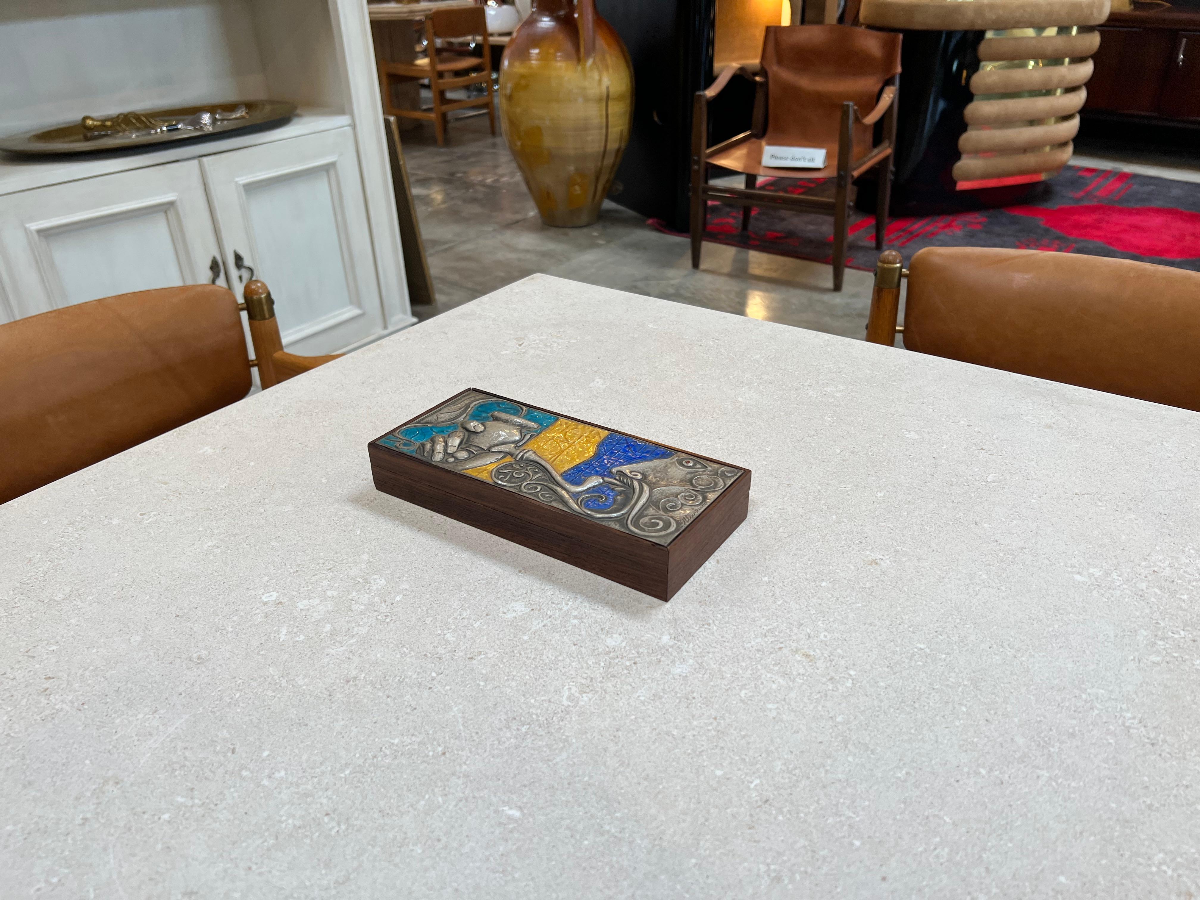 The Vintage Decorative Italian Wood Box from the 1980s is a charming and unique piece featuring a silver metal decoration on the top, adorned with blue and yellow accents. Crafted with exquisite Italian craftsmanship, this box serves as both a