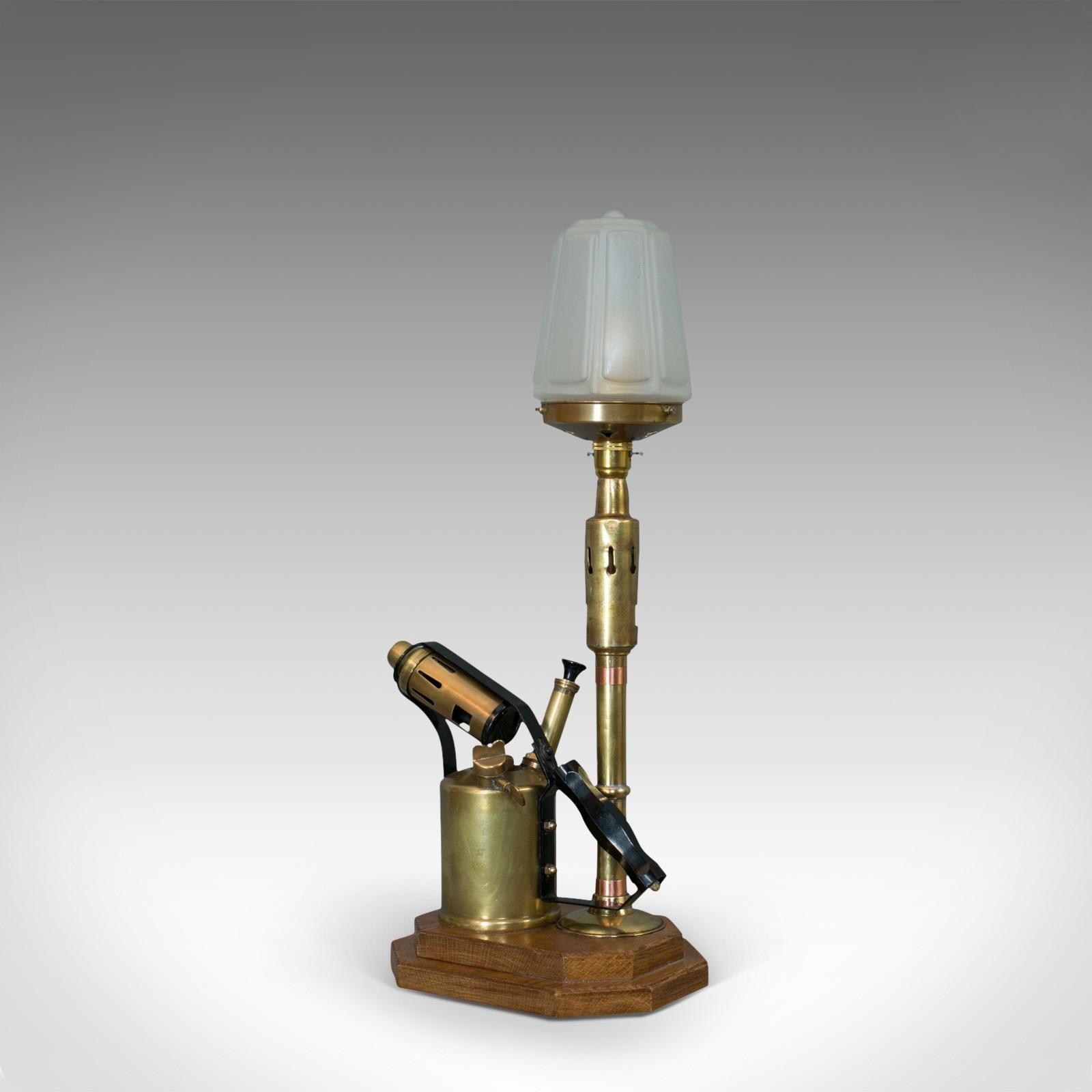 This is a vintage decorative lamp. An English, brass blow torch light with shade with oak base and dating to the 20th century.

Fascinating lamp with industrial appeal
In excellent condition, fully working with quality, opaque fluted lamp