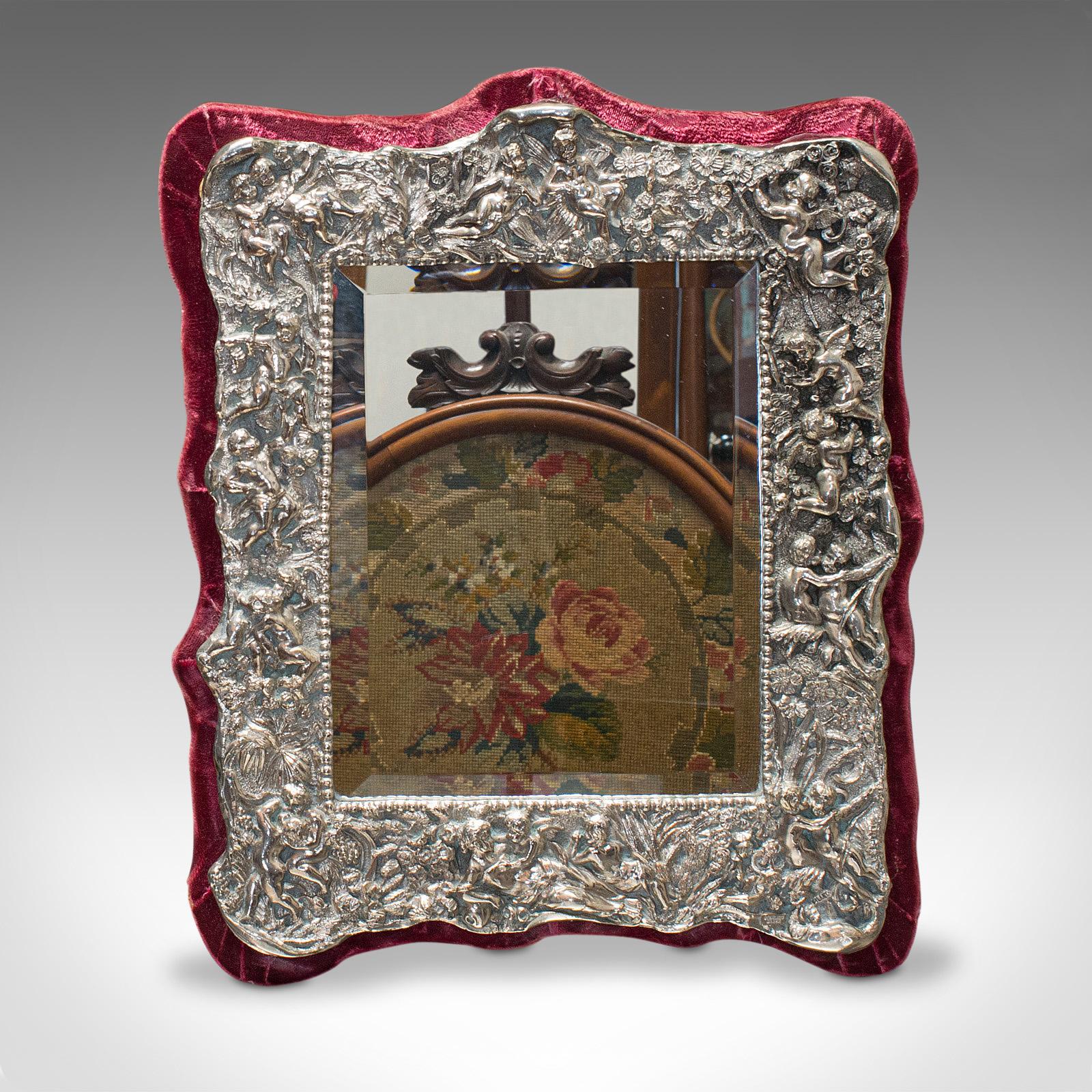 This is a vintage decorative mirror. An English, sterling silver and glass mirror, dating to the mid-20th century, circa 1950.

Ornate mirror frame with vibrant color
Displays a desirable aged patina
Sterling silver frame in good order
Original