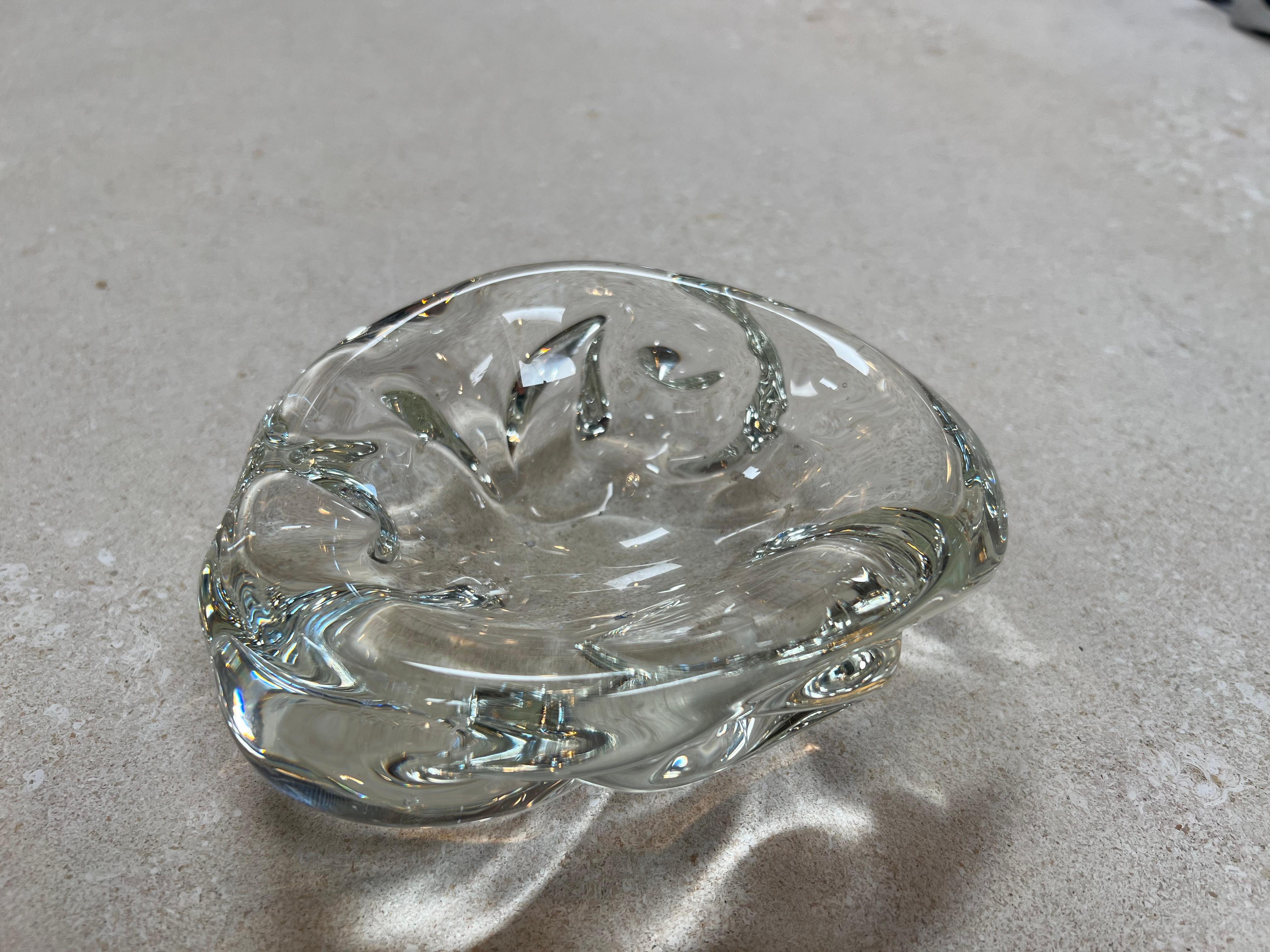 The Vintage Decorative Small Glass Shell Bowl from the 1960s exudes a delicate and charming aesthetic. Crafted in the shape of a shell, this bowl captures the essence of ocean-inspired beauty. The glass material lends it a sense of transparency and