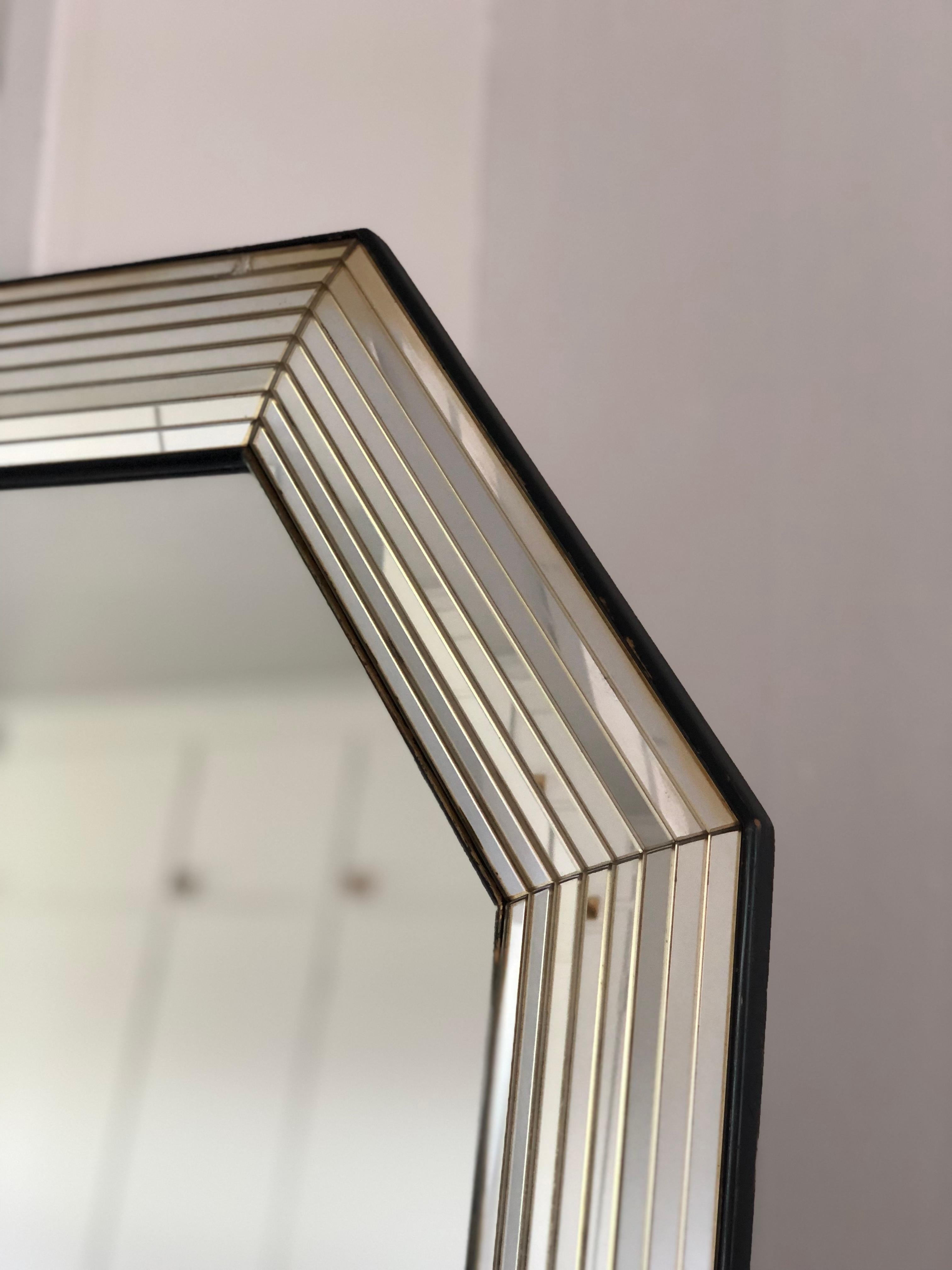 This octagon mirror by Deknudt, dating from the 1990s, is crafted in Belgium. The frame features a depth-formed glass design that runs across its entire width, creating a unique and elegant look. A black and silver strip surrounds the edges, adding