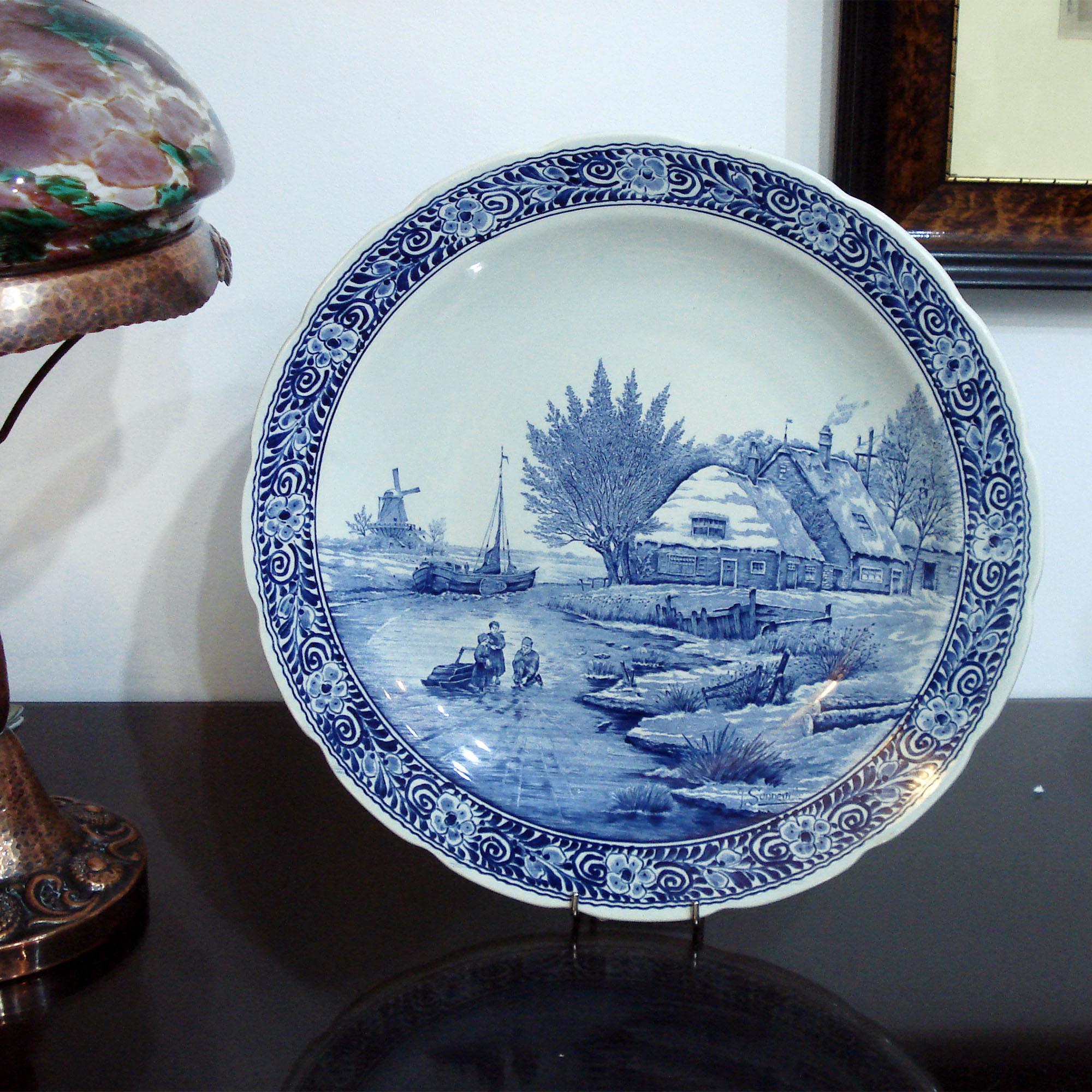 Vintage large wall hanging plate by Delfts Royal Sphinx. Hand painted decorative floral border, center design in transfer ware technique. Blue and white cottage scene, Dutch windmill and boat, people skating on the frozen lake. Hanging wire on the