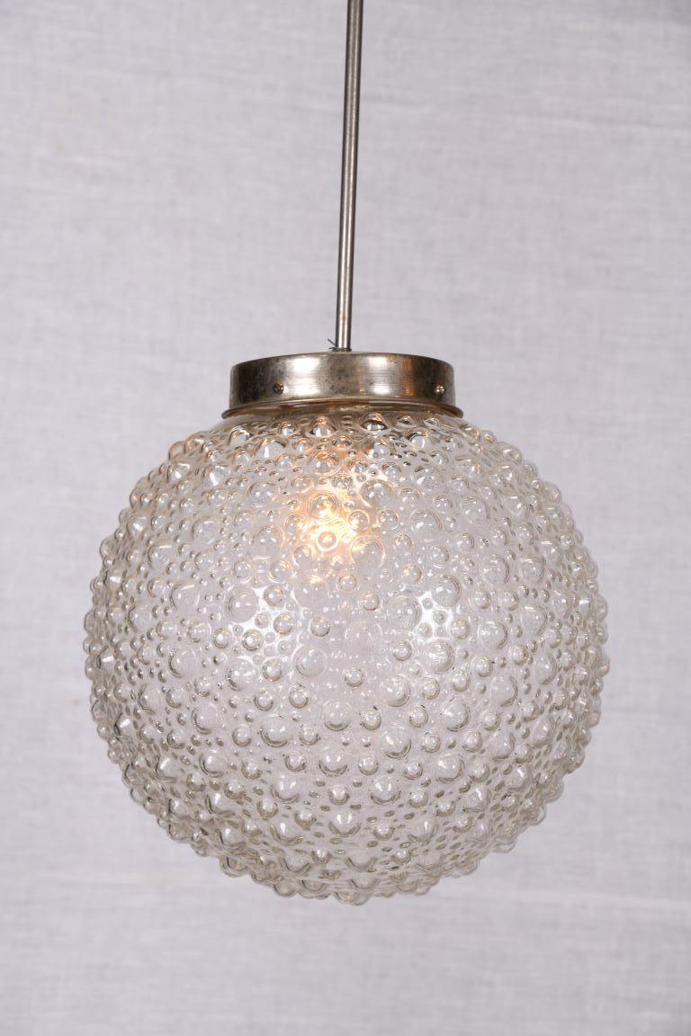 Prickelnd und frech! Extra große Kugel aus mundgeblasenem, strukturiertem Glas mit einem verchromten Rahmen.

Thomas Cooper Studio steht für eine vielschichtige, facettenreiche Collaboration, bei der sich Materialien und Techniken auf der Suche nach