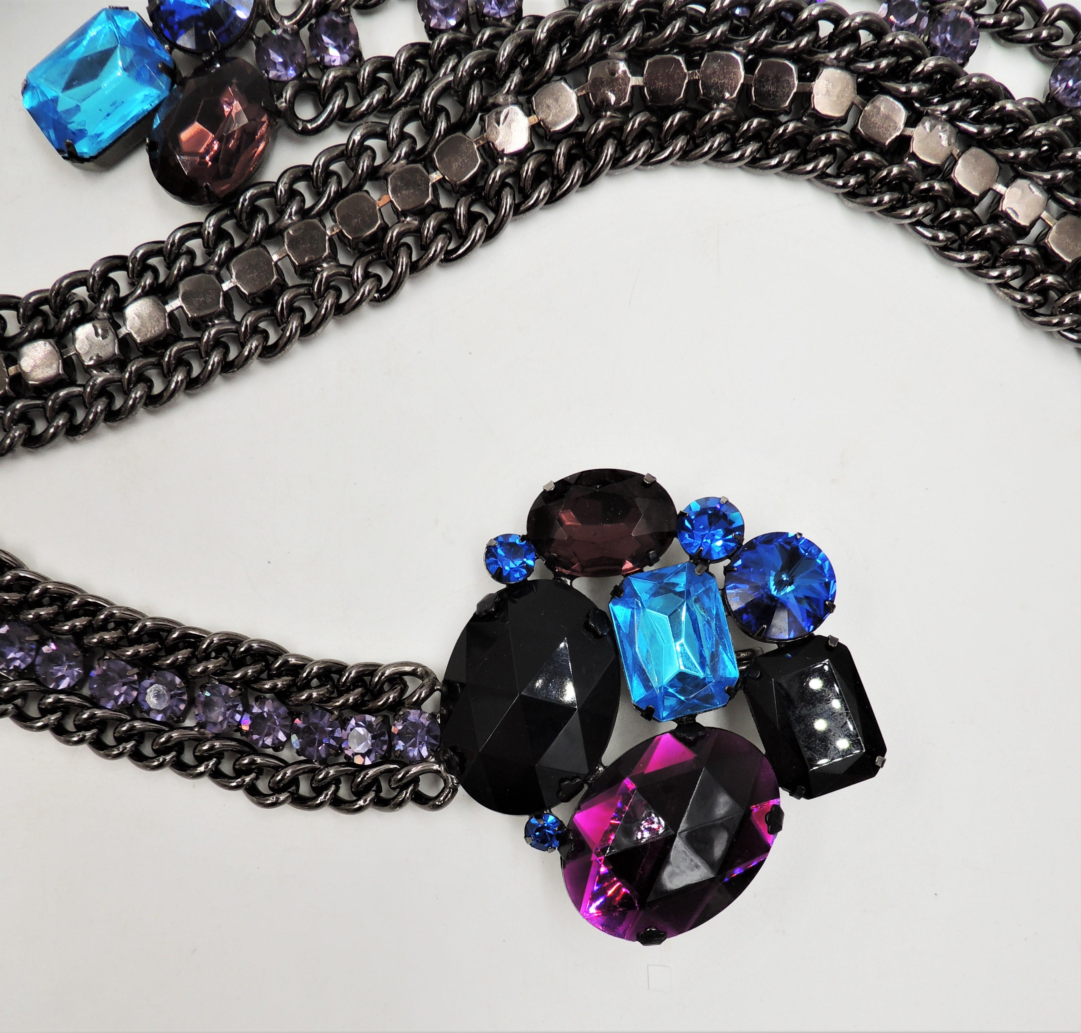 Blackened metal with huge prong set black, purple and blue faceted rhinestones with smaller prong set round faux-amethyst belt with hook clasp. The largest setting has a circumference of about 30 inches. Overall measures: 35 inches long. Large