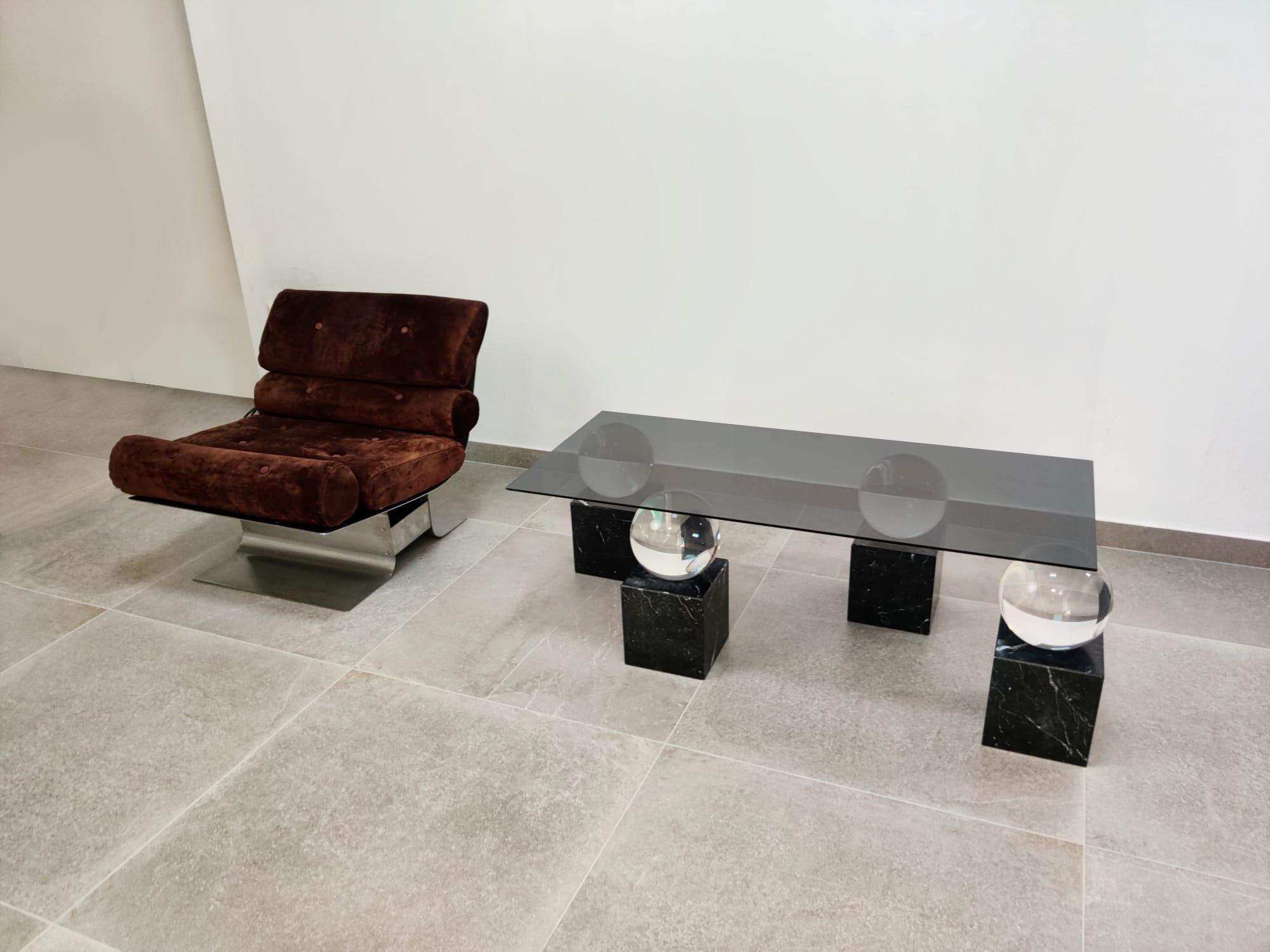 Table des années 1970 présentant un plateau en verre fumé soutenu par des sphères en acrylique et des bases carrées en marbre noir veiné de blanc.