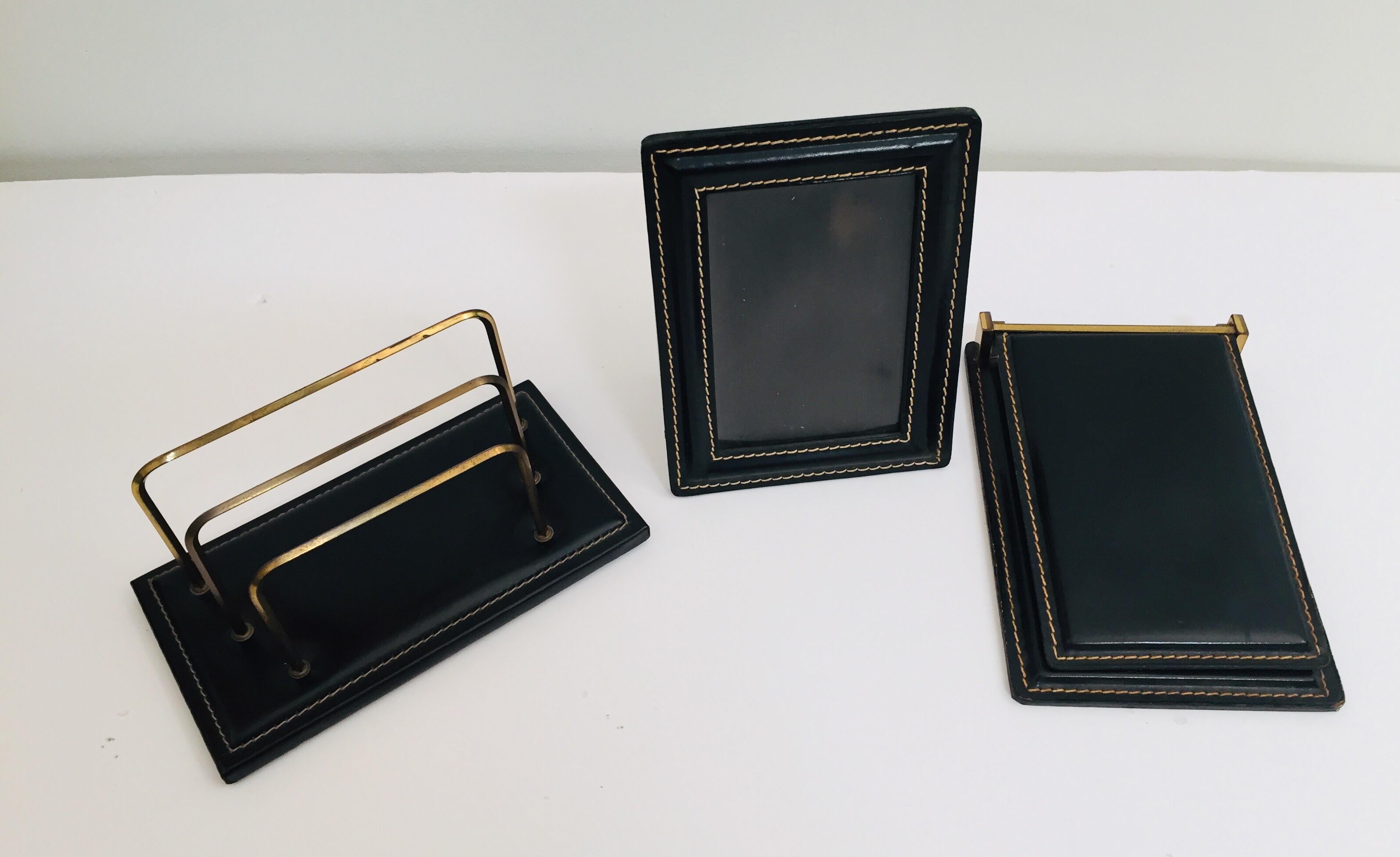 Adnet Art Deco style desk set comprising of a black leather and brass letter desk holder, rack, picture frame and a leather note pad with original paper refill and leather photo frame.
The leather with contrast saddle stitching is handcrafted and