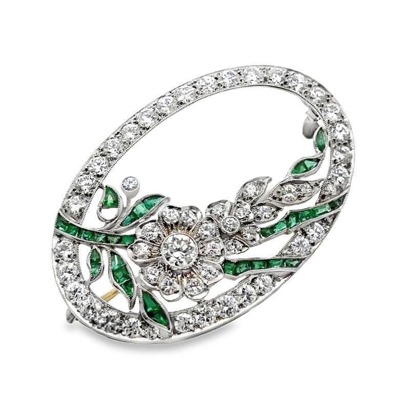 This elegant platinum flower brooch is set with approximately 2.10 carats of sparkling diamonds, mostly G-H/VS, and beautifully accented with calibre-cut emeralds. Measuring 1-5/8 x 1-1/8 inches and weighing 11.39 grams, this brooch showcases