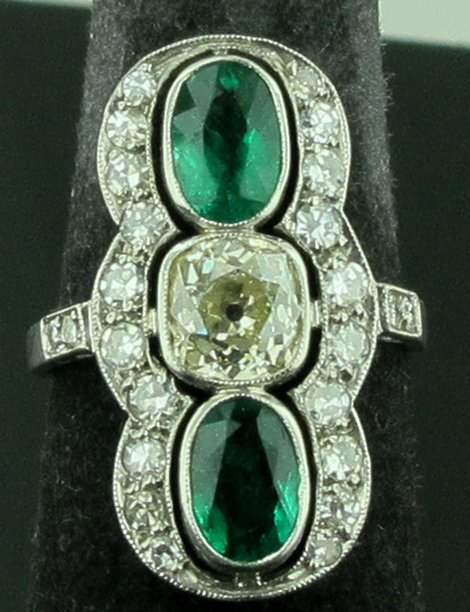 Circa 1910 Vintage Emerald and diamond ring set in Platinum. Ring features two oval shaped Emeralds with a carat weight of approximately 1 carat each, for a total of 2 carats.  The Center Old Mine Cut Diamond has a weight of 1.40 carats, K-L color,