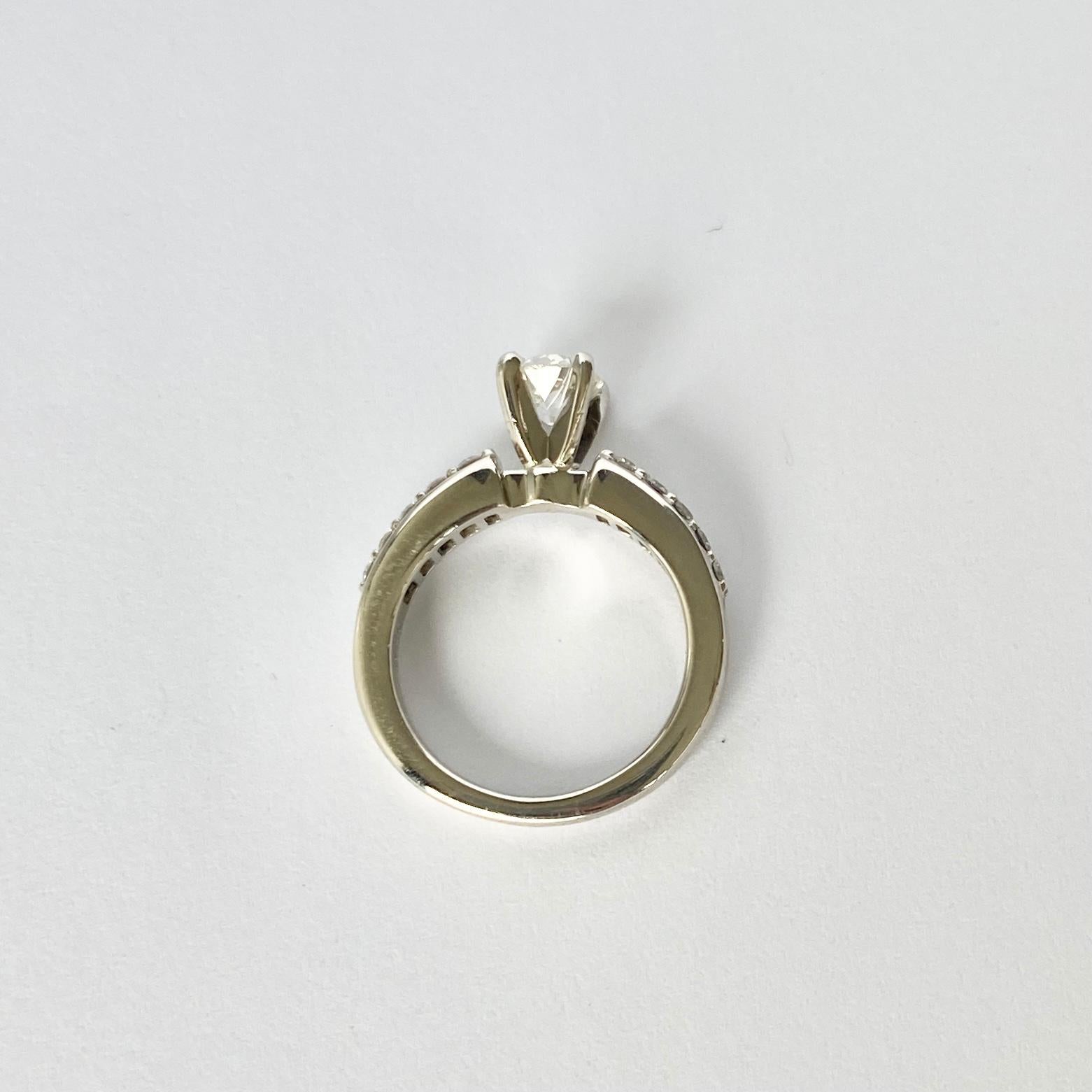 Der Hauptdiamant in diesem Ring misst 60 pt und hat die Farbe H/I. Der Stein glänzt wunderschön, und auf den Schultern sitzen auf jeder Seite fünf abgestufte Diamanten. Der Ring ist aus Platin modelliert. 

Ringgröße: H oder 3 3/4
Höhe ohne Finger: