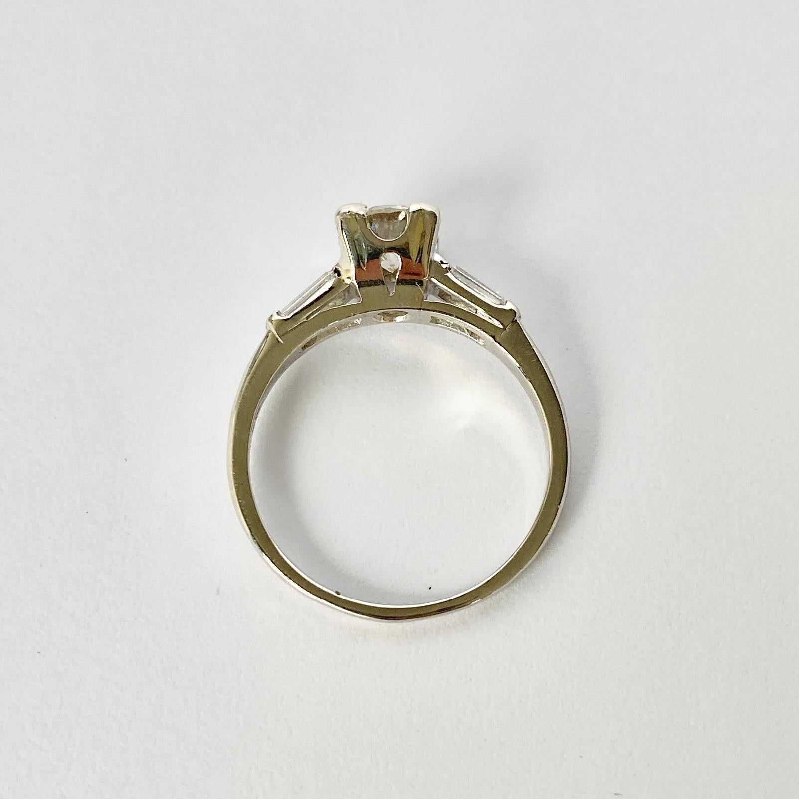 Der Hauptdiamant in diesem Ring misst 75 ppm und hat die Farbe H/I. Der Stein glänzt wunderschön und an den Schultern sitzen Baguette-Diamanten. Der Ring ist aus Platin modelliert. 

Ring Größe: M 1/2 oder 6 1/2 
Höhe ohne Finger: 6,5 mm

Gewicht: 4g