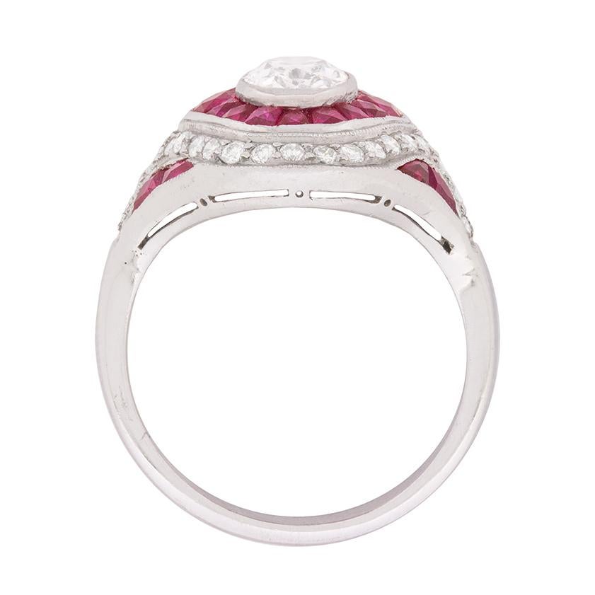 An Art Deco design influence is apparent in this sophisticated 1940s era diamond and ruby bombé style ring.

This stunning vintage ring centres a one carat, rubover set, oval-shaped diamond within a rich, rubover set border of 0.70 carat French cut