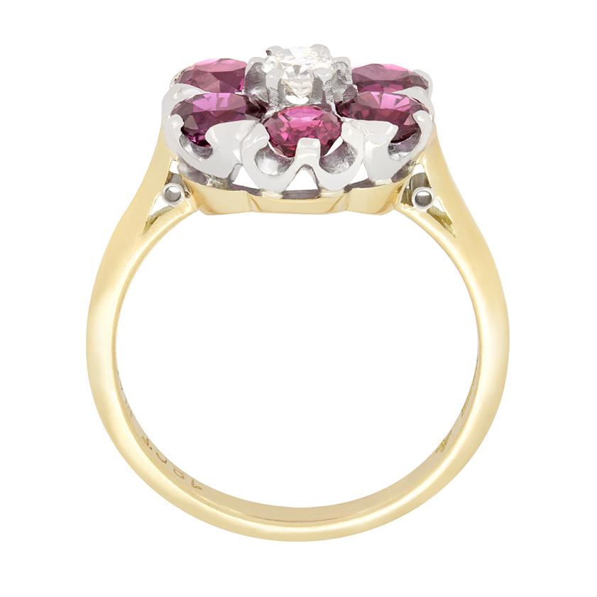 Dieser charaktervolle Blumenring im Vintage-Stil zeigt einen zentralen Diamanten, der von Rubinen im Ovalschliff umgeben ist. Der Diamant im Übergangsschliff wiegt 0,20 Karat mit einer Farbe von G und einer Reinheit von VS. Die umliegenden Rubine