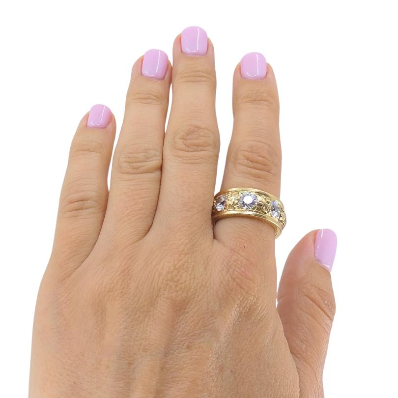 This vintage 14k gold band features a detailed leaf motif that makes a textured backdrop for its diamond accents. Three larger diamonds are spaced evenly across the center of the ring. Five smaller diamonds are set within the organic pattern at the