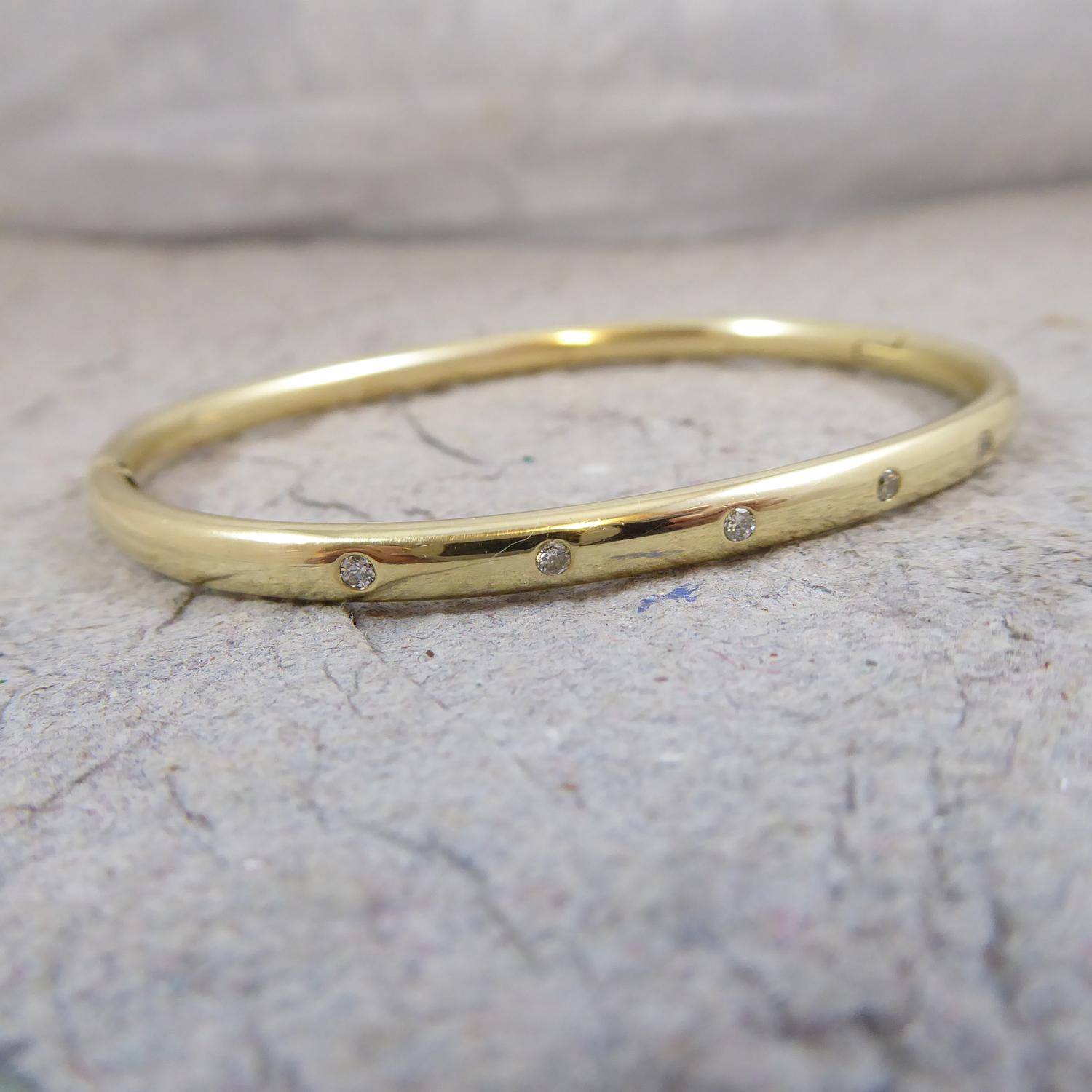 A contemporary, pre-owned bangle in 9ct yellow gold.  Set to the front half with six round brilliant cut diamonds approx. 0.12ct in total.  The bangle is oval shaped and fastens with a V spring clip catch. Measuring 0.16 inch (4.0mm) wide.  Internal