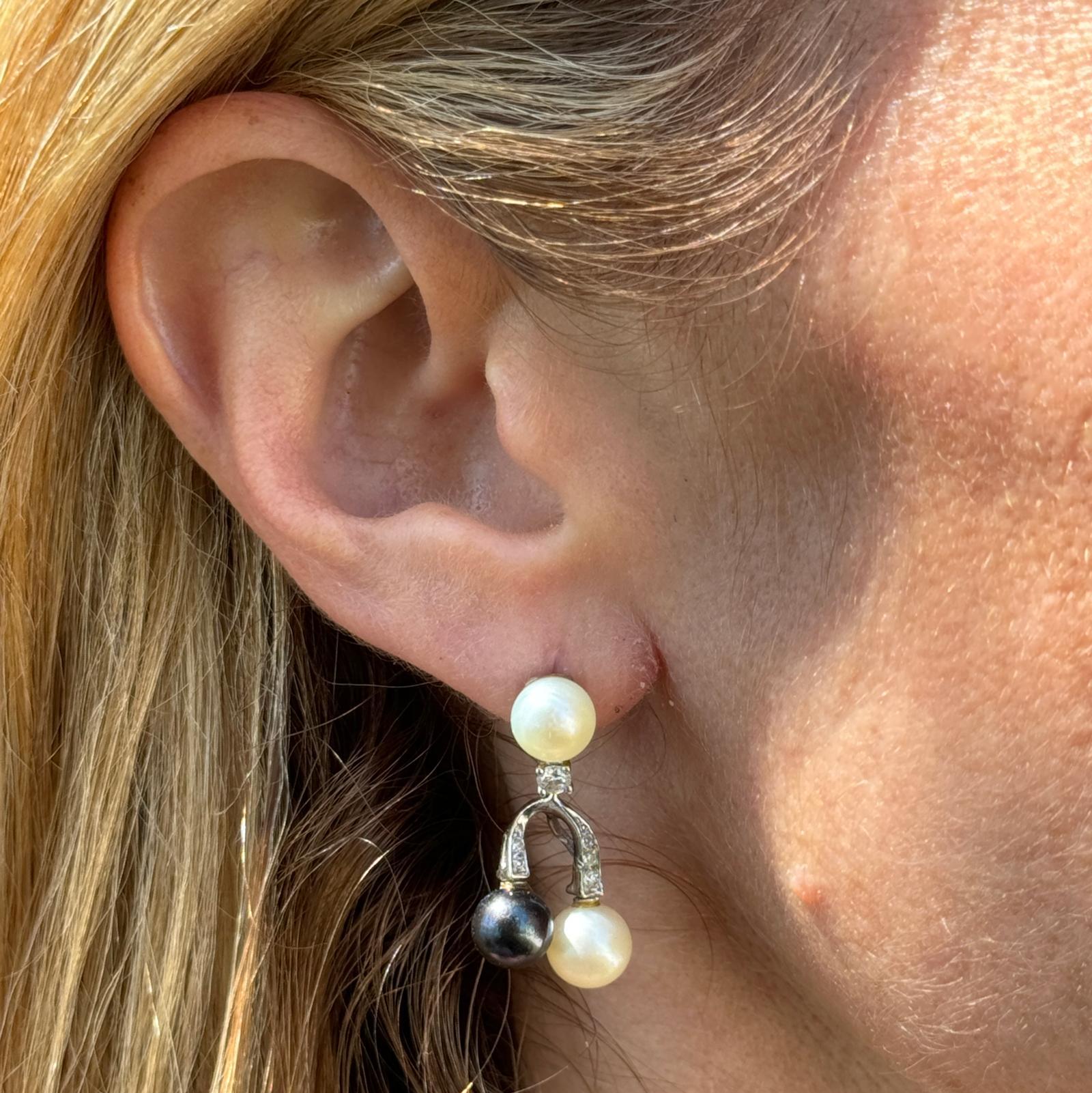 Black and white pearl diamond dangle vintage earrings crafted in 14 karat white gold. The earrings feature 7mm white and black pearls, 2 round brilliant cut diamonds and 10 single cut diamonds weighing approximately .30 carat total weight. The