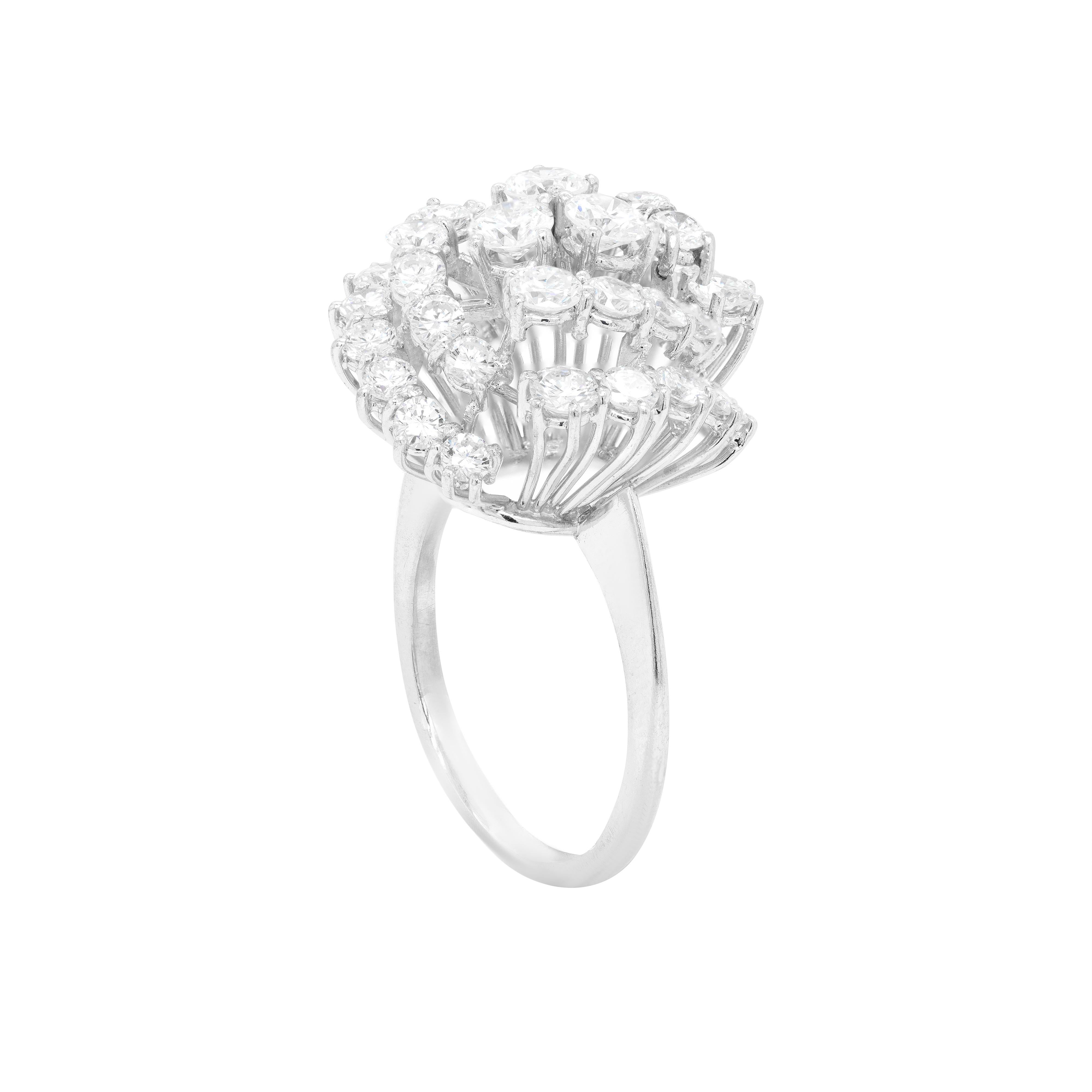 This gorgeous 18 carat white gold vintage ring is beautifully centred with 3 round brilliant cut diamonds, mounted in four claw, open back settings. Surrounding the centre stones there are three cascading asymmetrical swirls, each beautifully set