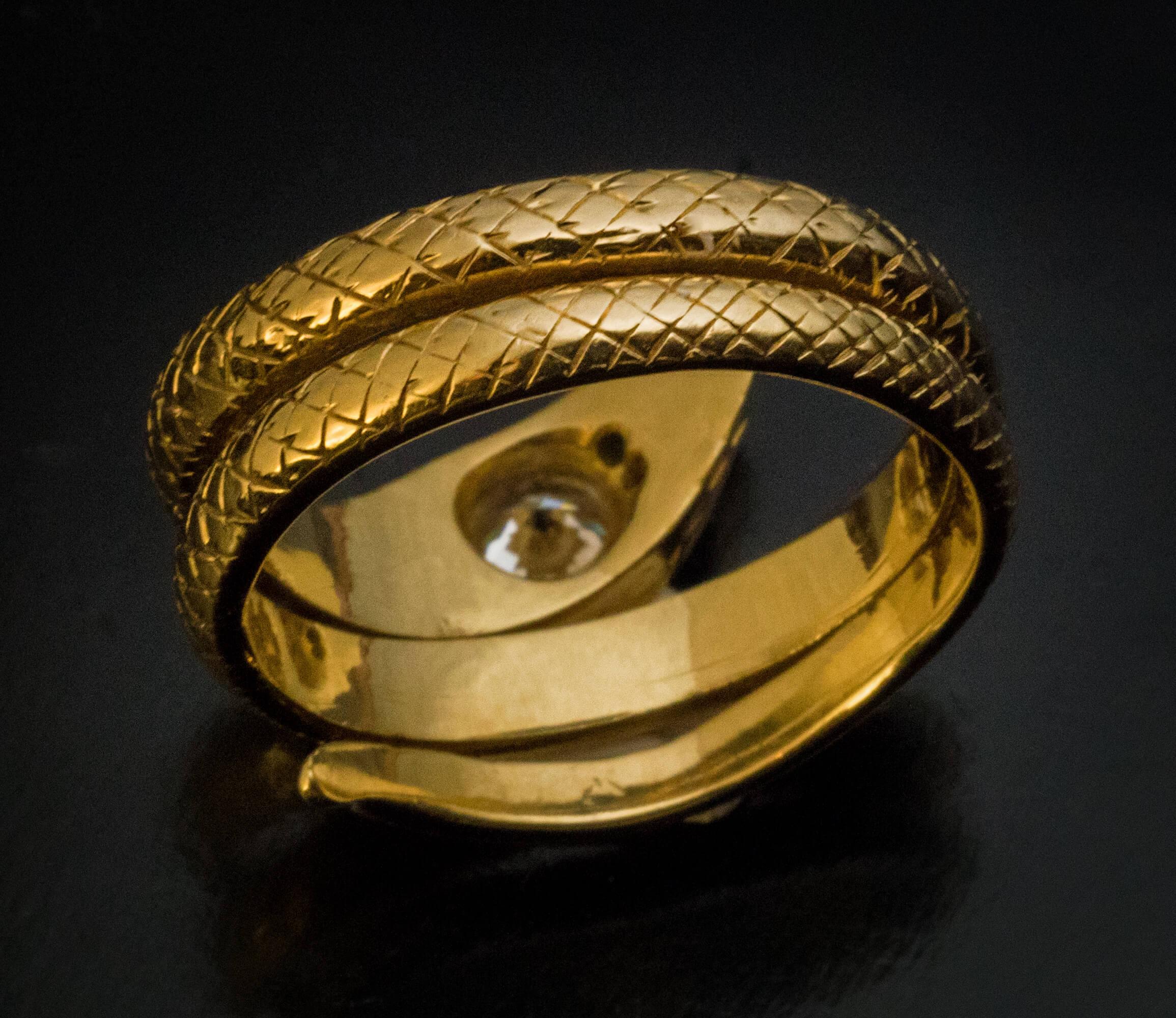 This solid 18K gold ring is designed as a stylized coiled snake with finely hand-engraved skin.  The head of the snake is embellished with a sparkling bright white diamond (approximately 0.51 ct, H color, VS1 clarity). The eyes are set with small