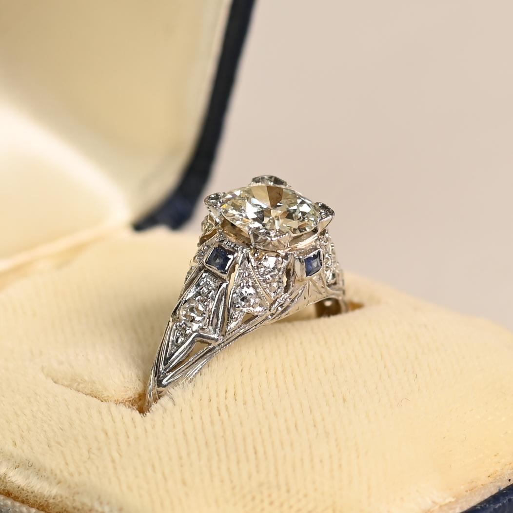 Dieser exquisite originale Art-Déco-Verlobungsring präsentiert einen fesselnden, ca. 1,2 Karat schweren Diamanten im alten europäischen Schliff, mit der Graduierung J in der Farbe und SI2 in der Reinheit. Der Diamant in der Mitte ist elegant in