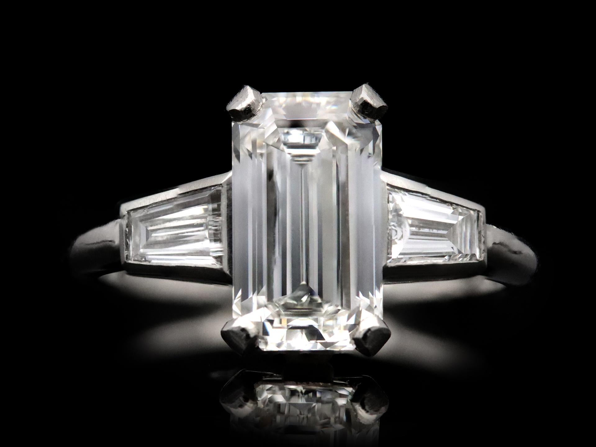 Vintage diamond flanked solitaire ring. Set to centre with an octagonal emerald-cut diamond, F colour, VVS2 clarity, with a weight of 2.22 carats in an open back claw setting, flanked by two tapered baguette cut diamonds in open back rubover