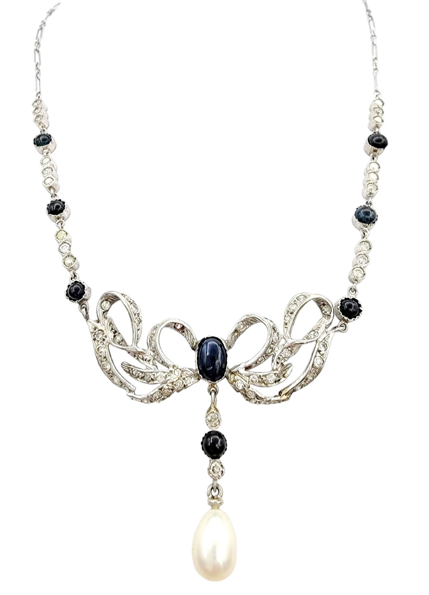 This vintage platinum pendant necklace is a masterpiece of elegance and sophistication, featuring a captivating arrangement of precious gemstones. The central bow designed pendant is adorned with lustrous cabochon sapphires, which adds a rich and