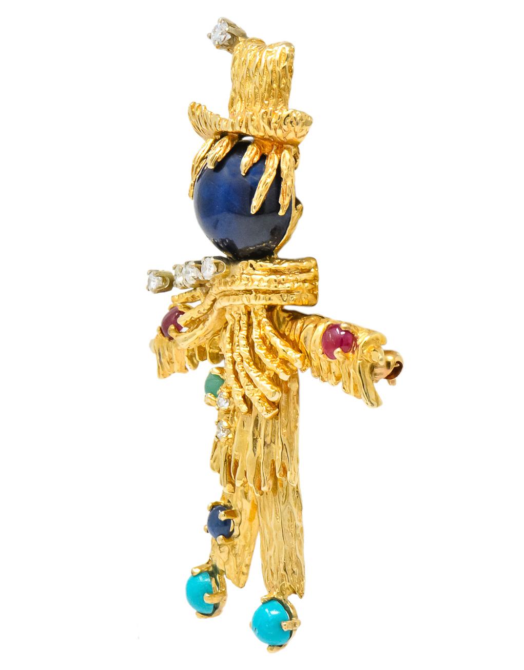 Articulated scarecrow designed as a round cabochon cut sapphire head measuring 11.8 mm with textured gold clothing, hat, and scarf

Set throughout by round cabochon cut emerald, sapphire, ruby, and turquoise

Accented by round brilliant cut