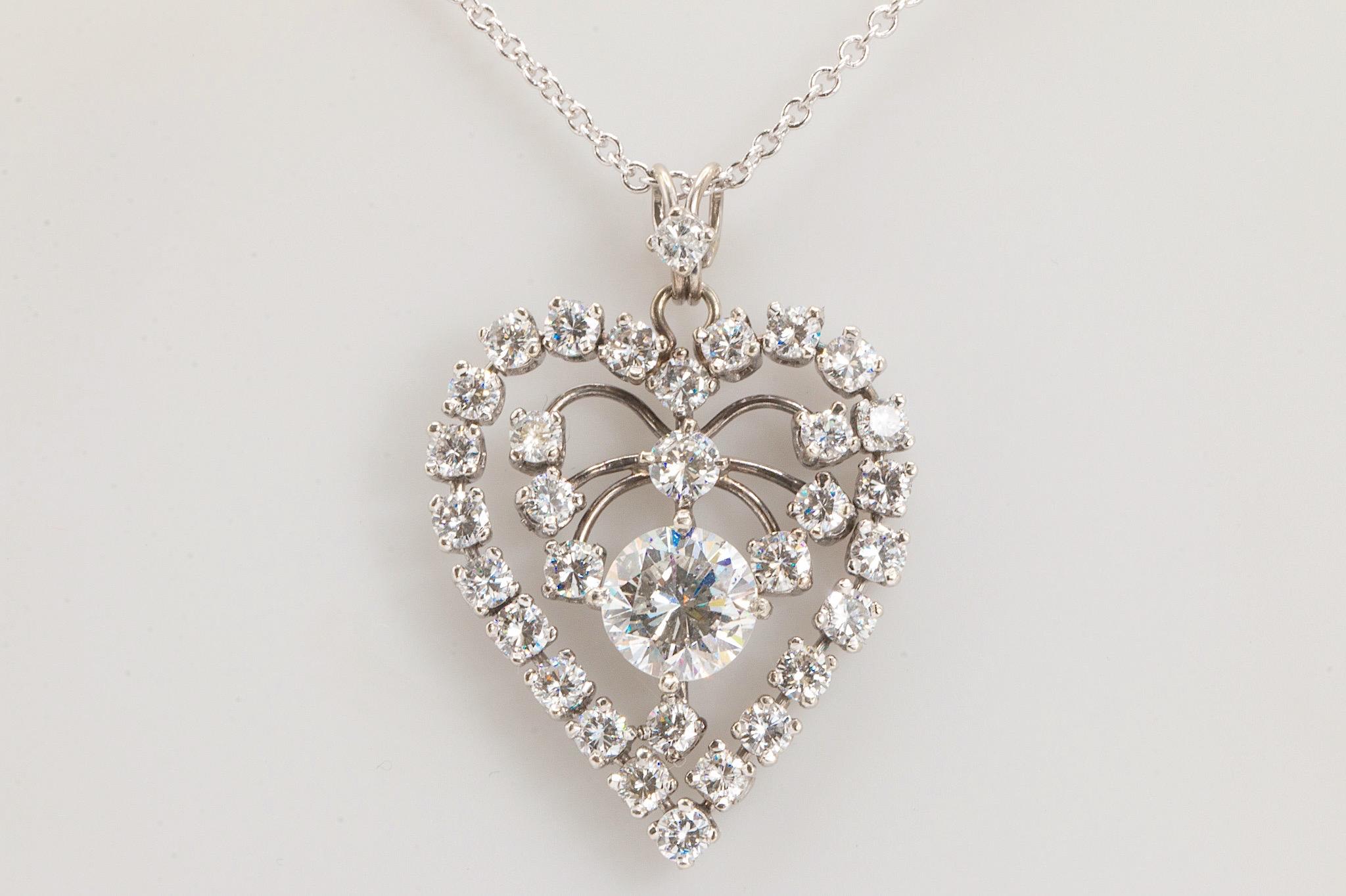 A stunning vintage 14K white gold heart pendant, adorned with 32 round brilliant diamonds totaling approximately 3.25 carats. These diamonds exhibit exceptional E-G color and VS clarity. The centerpiece is a 1.89 ct. round brilliant diamond,