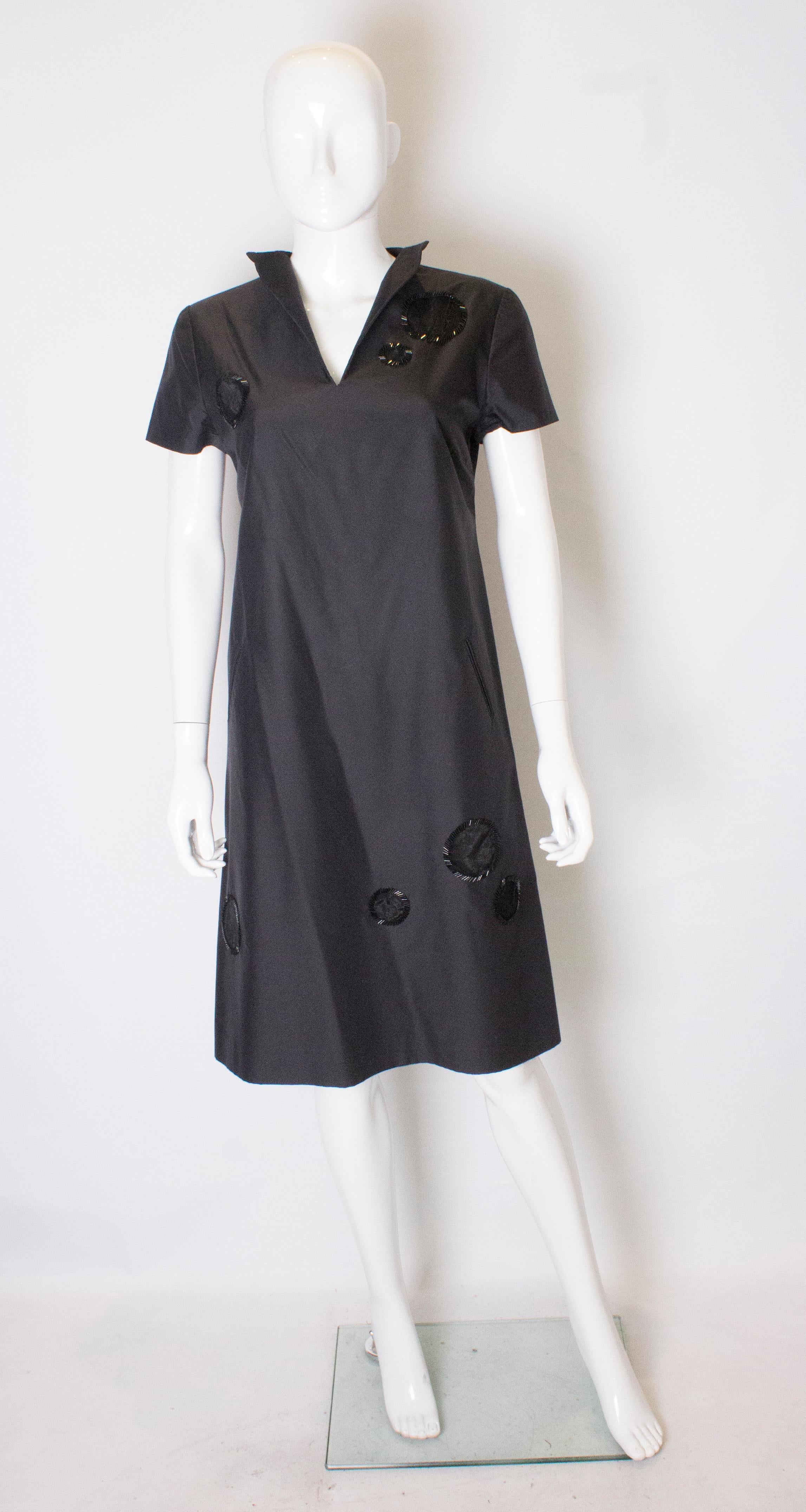 A chic cocktail dress by Didier Ludot , Paris. The dress has a deep v neckline, short sleaves, two pocketss at the front, and is decorated with bead edged circles. It is fully ined and has a central back zip.