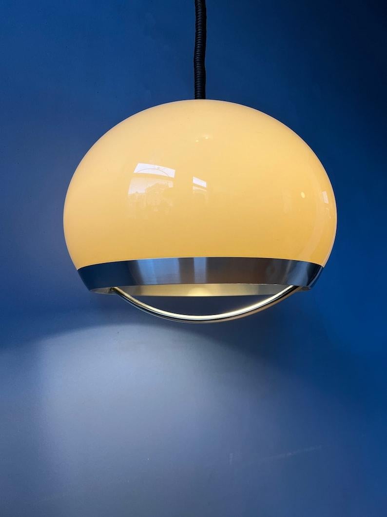 Beautiful space age pendant by Dijkstra in beige/mocca colour and aluminium/metal frame. The shade produces a magnificent glow, reflecting nicely on the chrome arc underneath the shade. The lamps requires an E27/26 (standard) lightbulb.

Additional