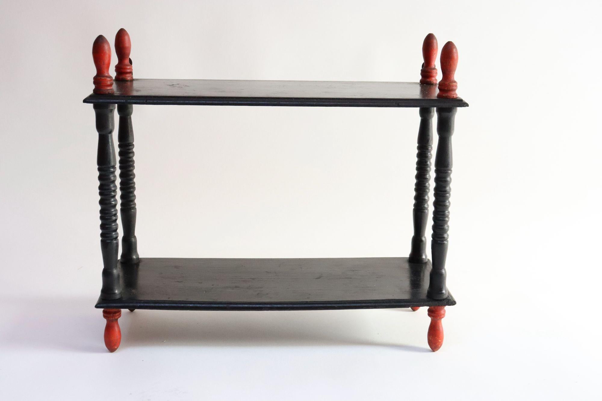 Charmantes Regal, bestehend aus einem geschnitzten Holzrahmen, der seinen ursprünglichen schwarzen Lack mit eleganten roten Endstücken/Füßen beibehält (ca. 1920er Jahre, USA).
Auf der Rückseite befinden sich zwei Metallklammern zur Befestigung, aber