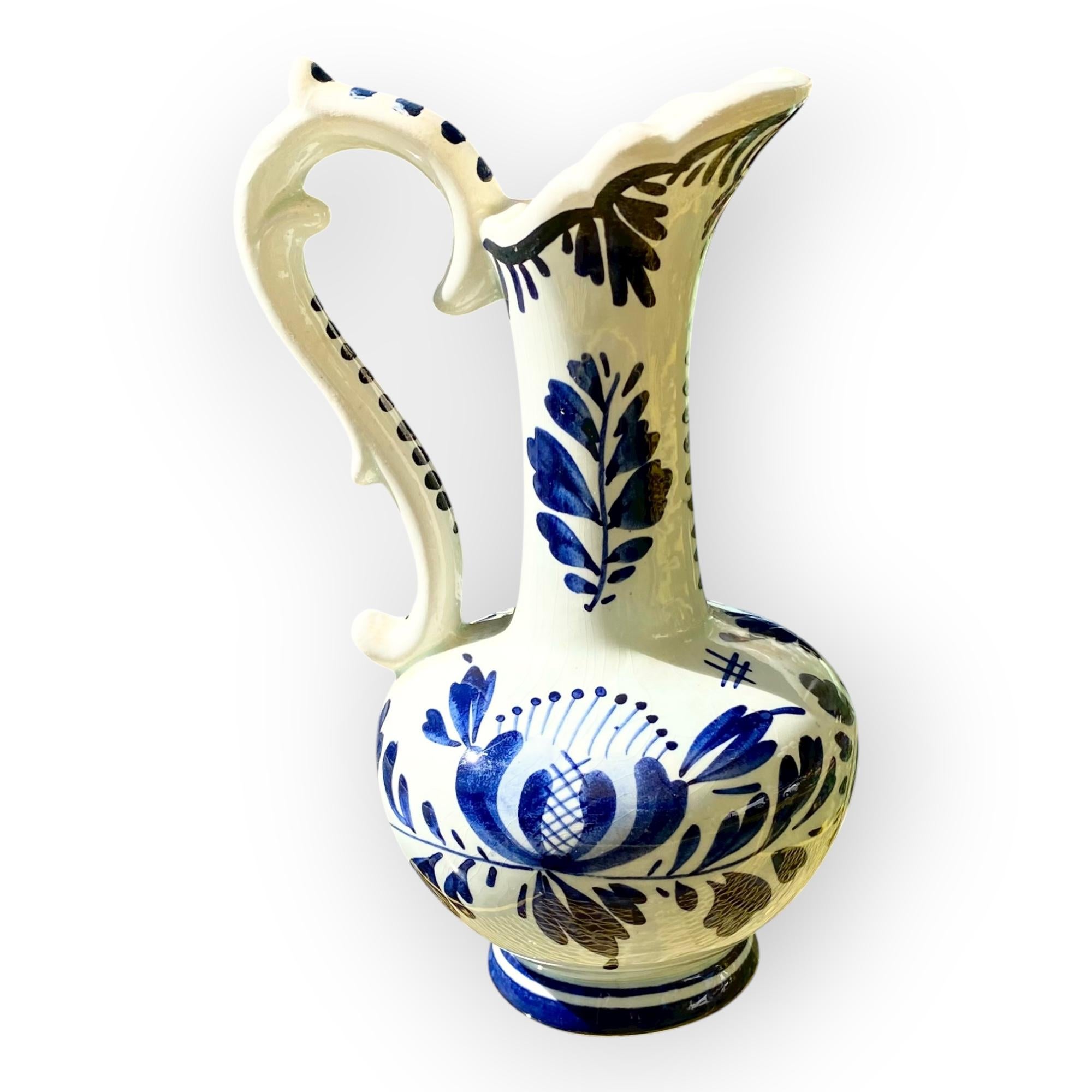 Bringen Sie einen Hauch von holländischer Eleganz und Tradition in Ihr Zuhause mit diesem raffinierten Vintage Delft Krug, einem authentischen Kunstwerk aus handbemalter Keramik in klassischem Weiß und Kobaltblau. Die dekorativen Motive, die in