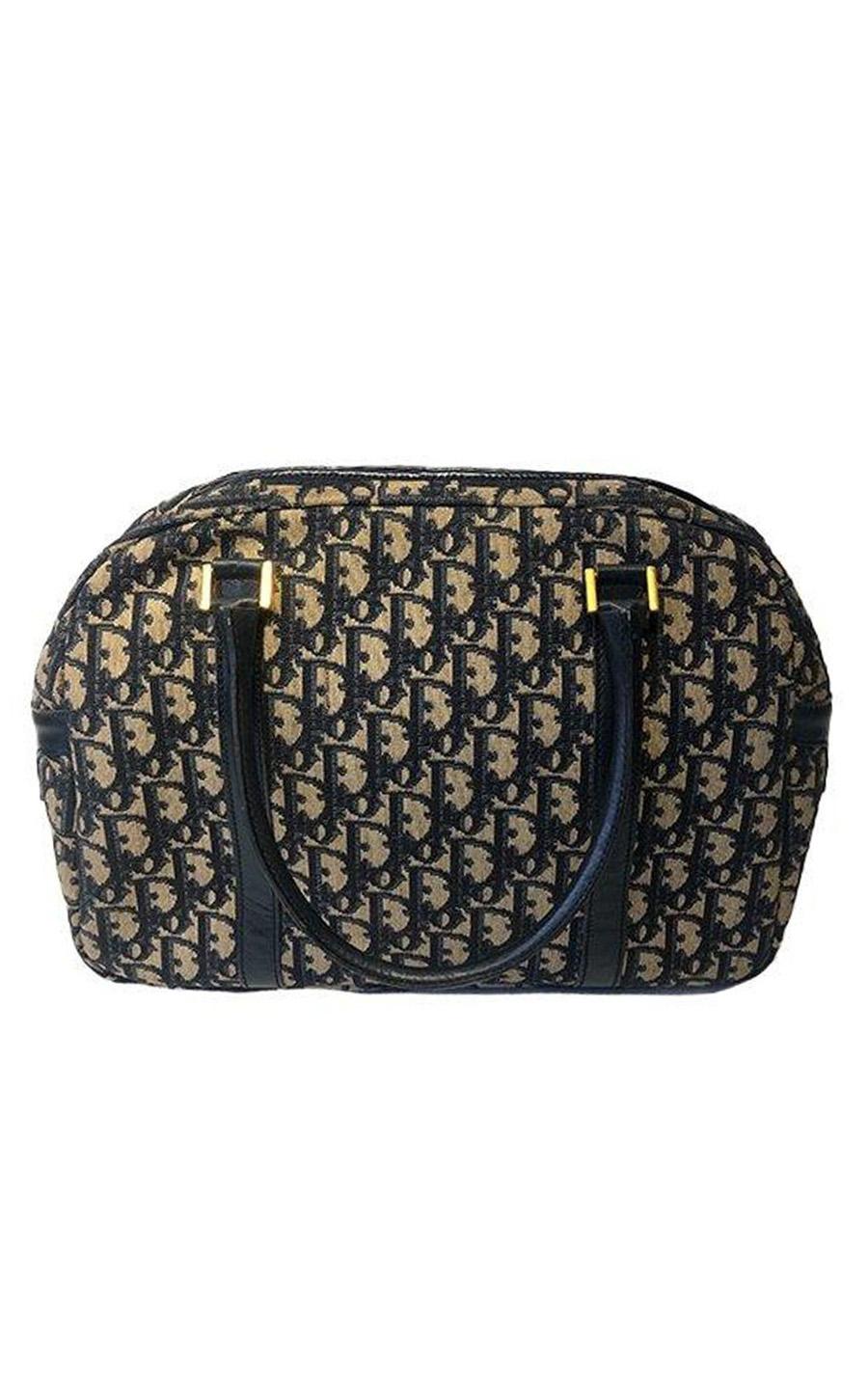 Dior handbag in the classic Dior-Oblique canvas. The bag is colored beige and dark blue. The hardware is gold-colored. The main compartment closes with a zipper, which contains a gold-colored Dior pendant and inside there are 2 slide in pockets. The