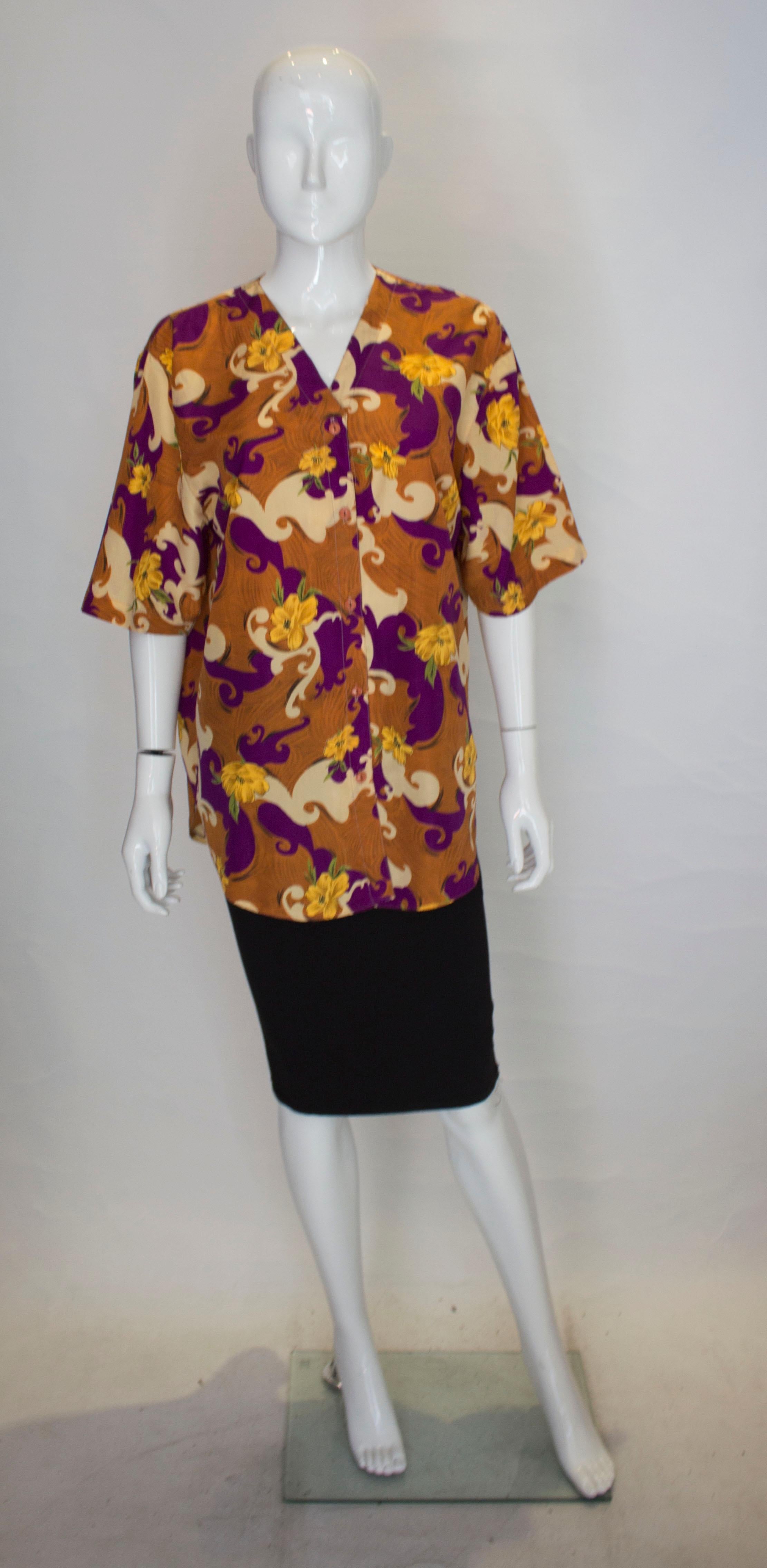 A fun silk blouse by Dior. The blouse is loose fitting with a v neckline , and button front. it has a brown background with a purple, yellow and cream design.