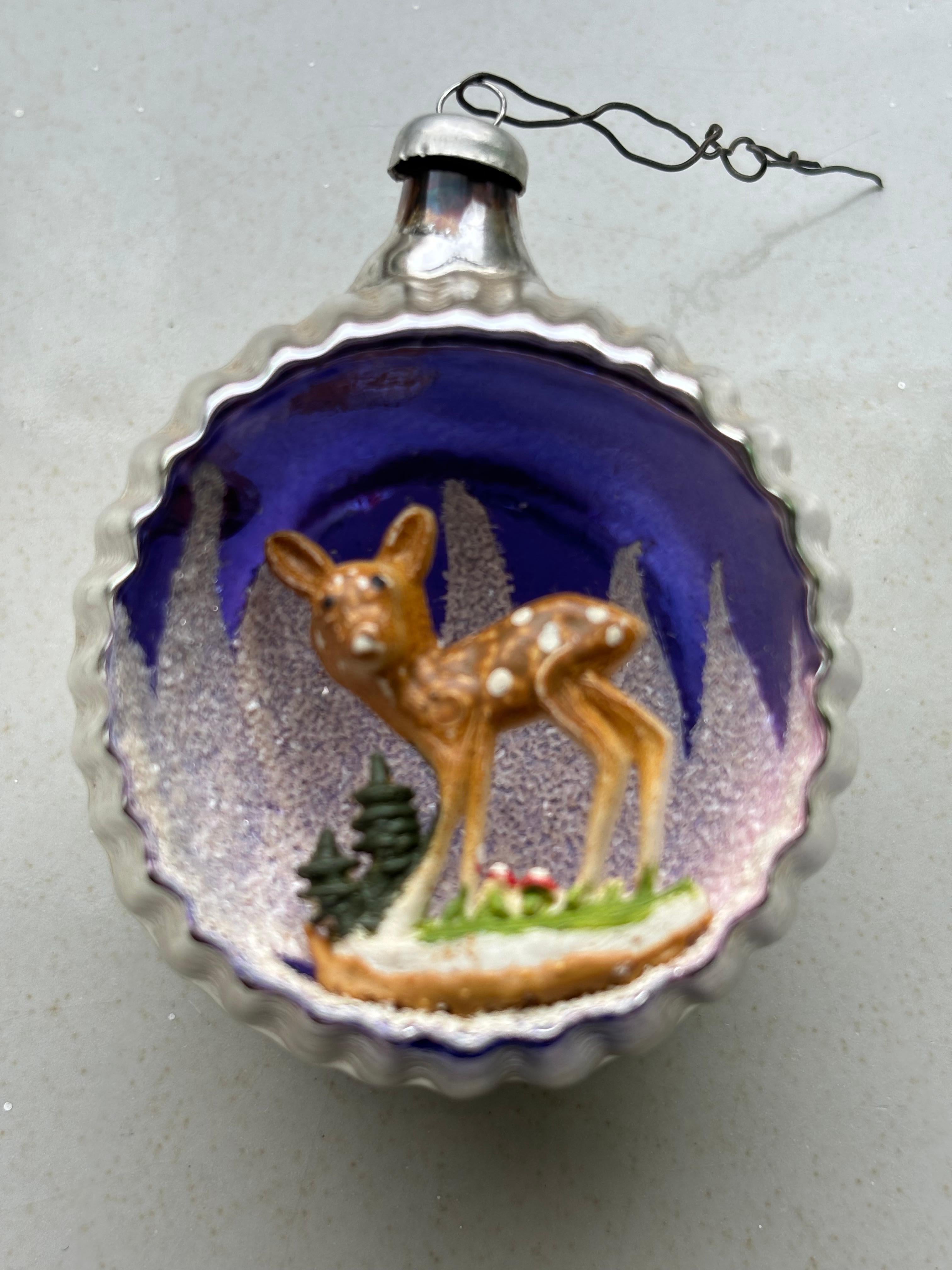 A perfect addition to your vintage themed Christmas tree or a great gift for the ornament collector! This diorama ornament features a flocked Purple, White/Pink background with a plastic deer, trees, and mushrooms over silver mercury glass. It