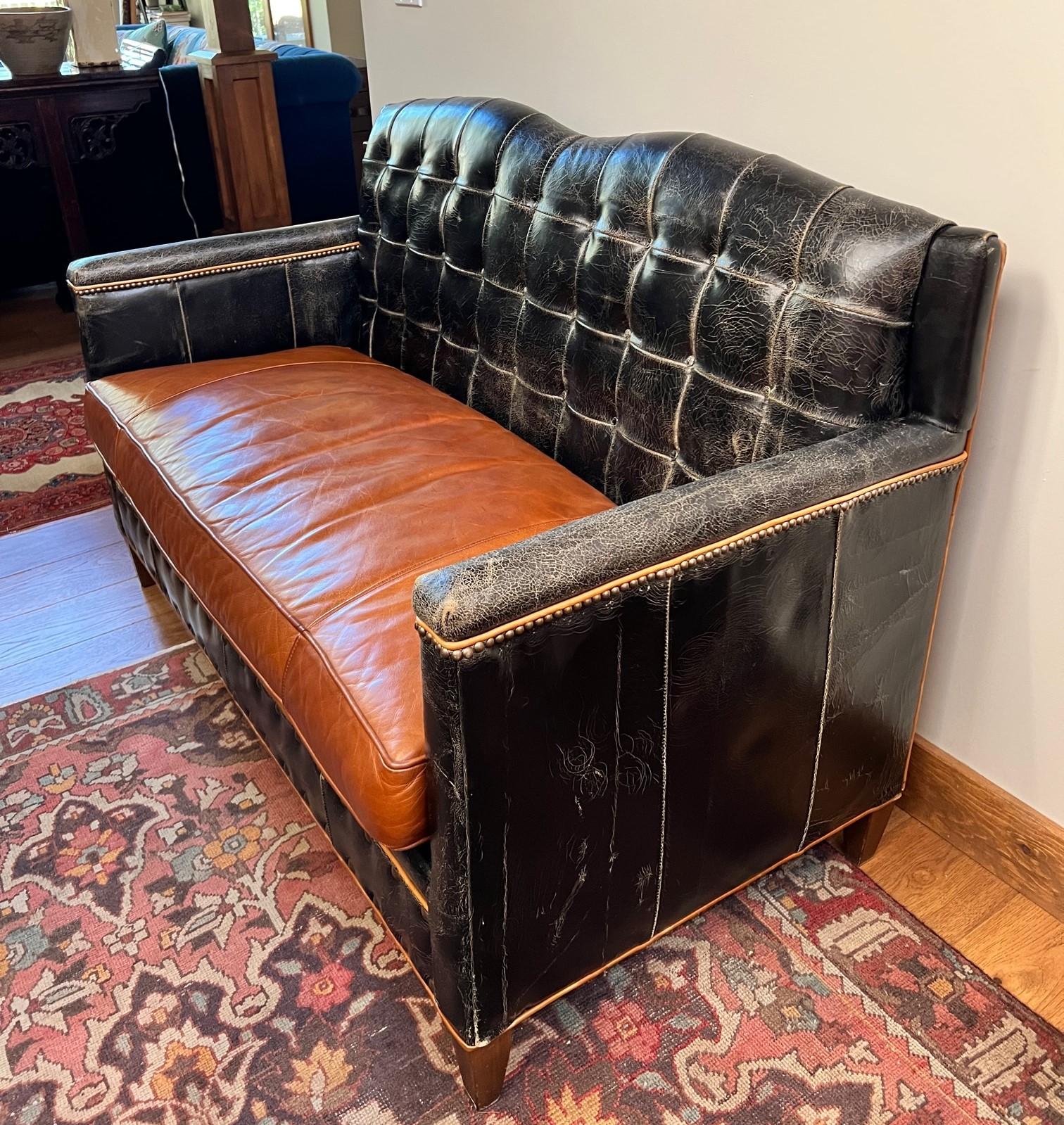 Vintage sofa/loveseat in deliberately distressed black leather with a caramel leather seat, piping and nail head trim.  The button tufting is very geometric and is only on the sofa back. The remaining leather is in panels. The sofa is raised on