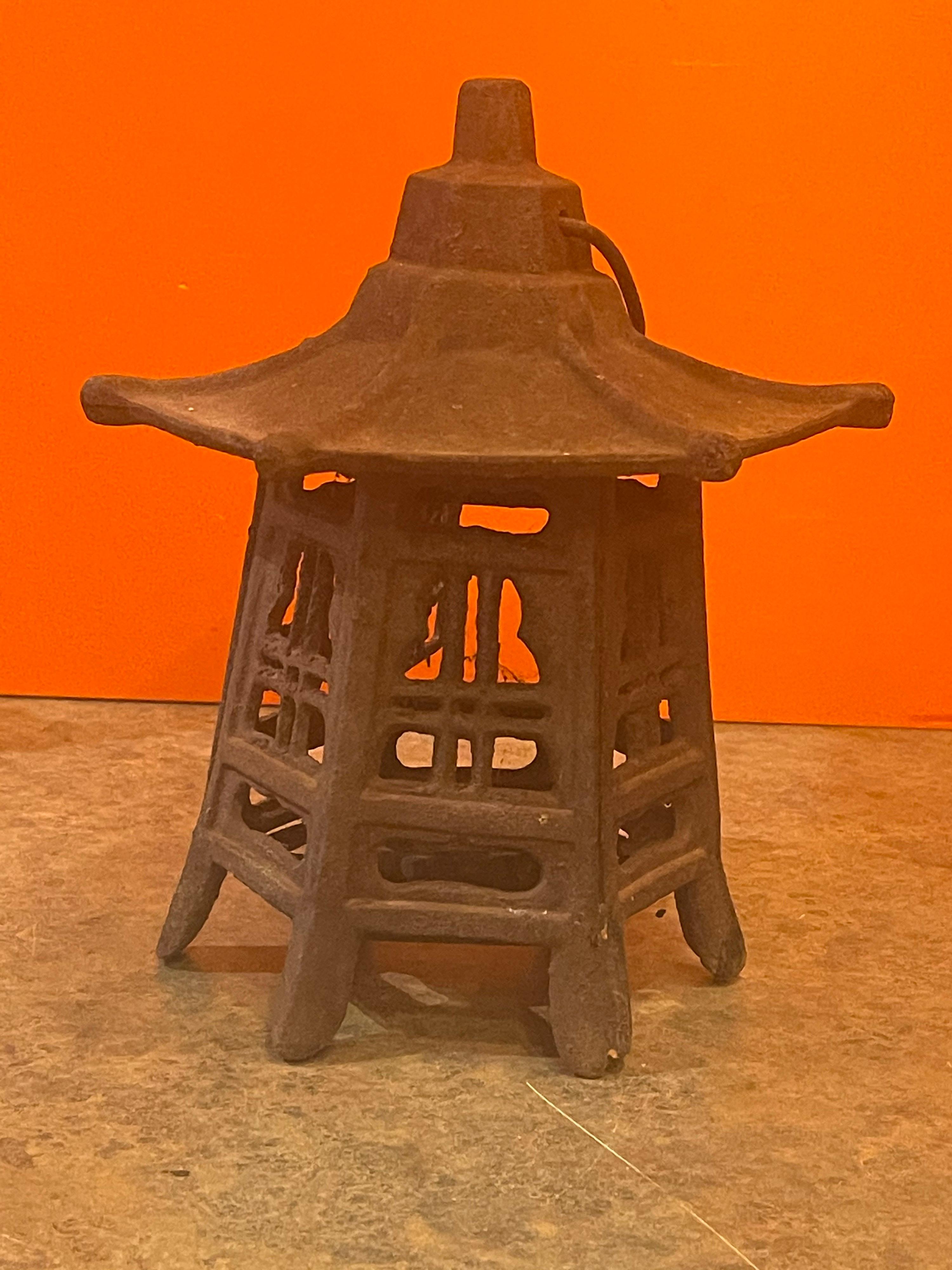Vintage distressed cast iron Japanese pagoda lantern, circa 1950s. The lantern has a great distressed rust patina and a wonderful look. The piece is solid and functional and has a small door that opens to allow a candle to be inserted. The pagoda is