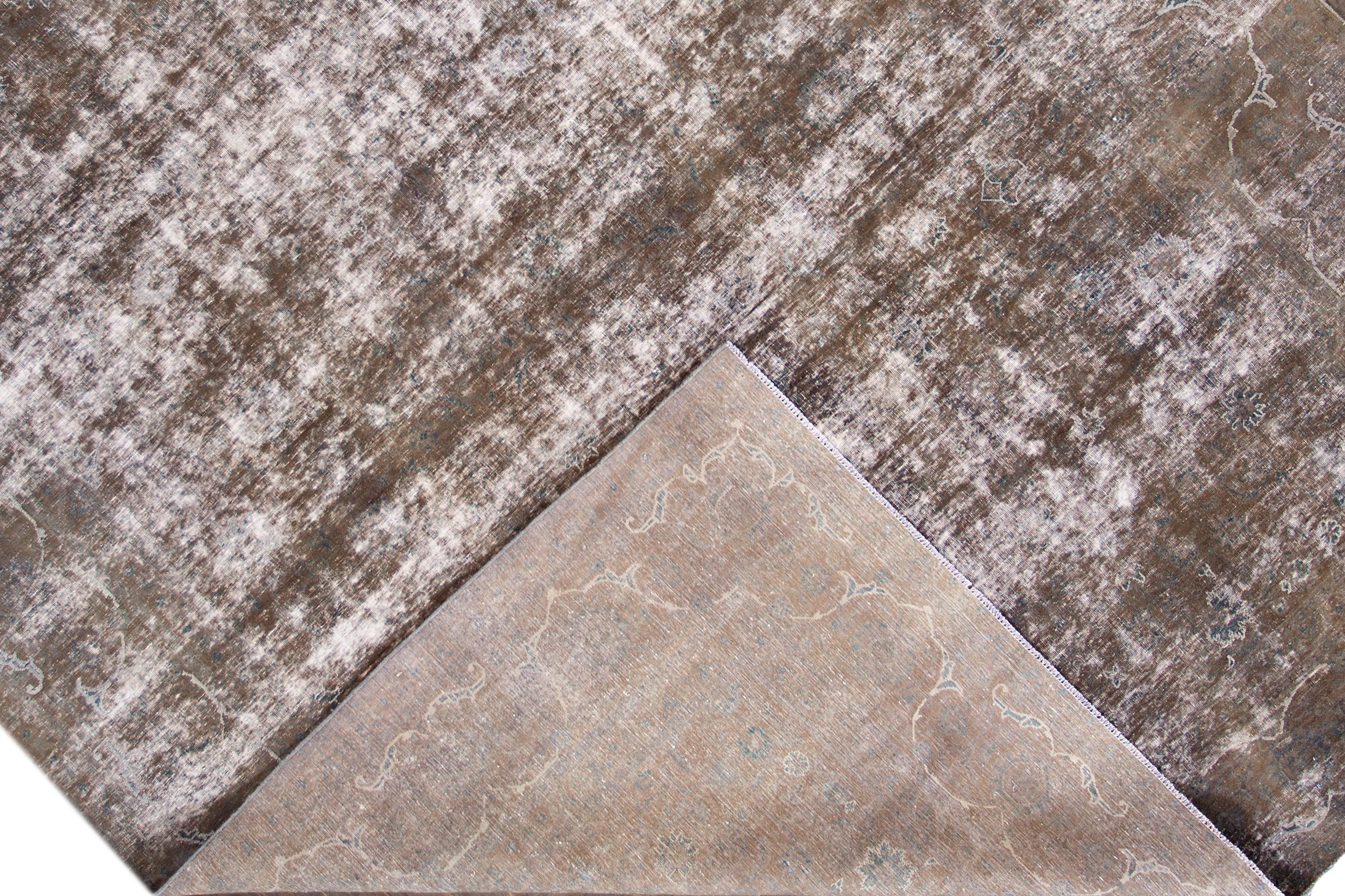 A mid-20th century vintage distressed Persian area rug with a taupe field and subtle all-over floral design. This hand knotted wool rug measures 9'3