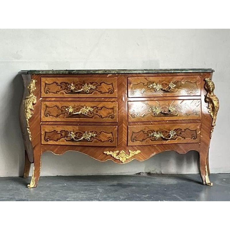 Questa spettacolare commode d'epoca cattura lo spirito sontuoso dello stile Rococo Luigi XV francese, mostrando una squisita silhouette a bombe (gonfiata). Il corpo è riccamente ornato da intricati motivi di intarsio e impiallacciatura, con curve