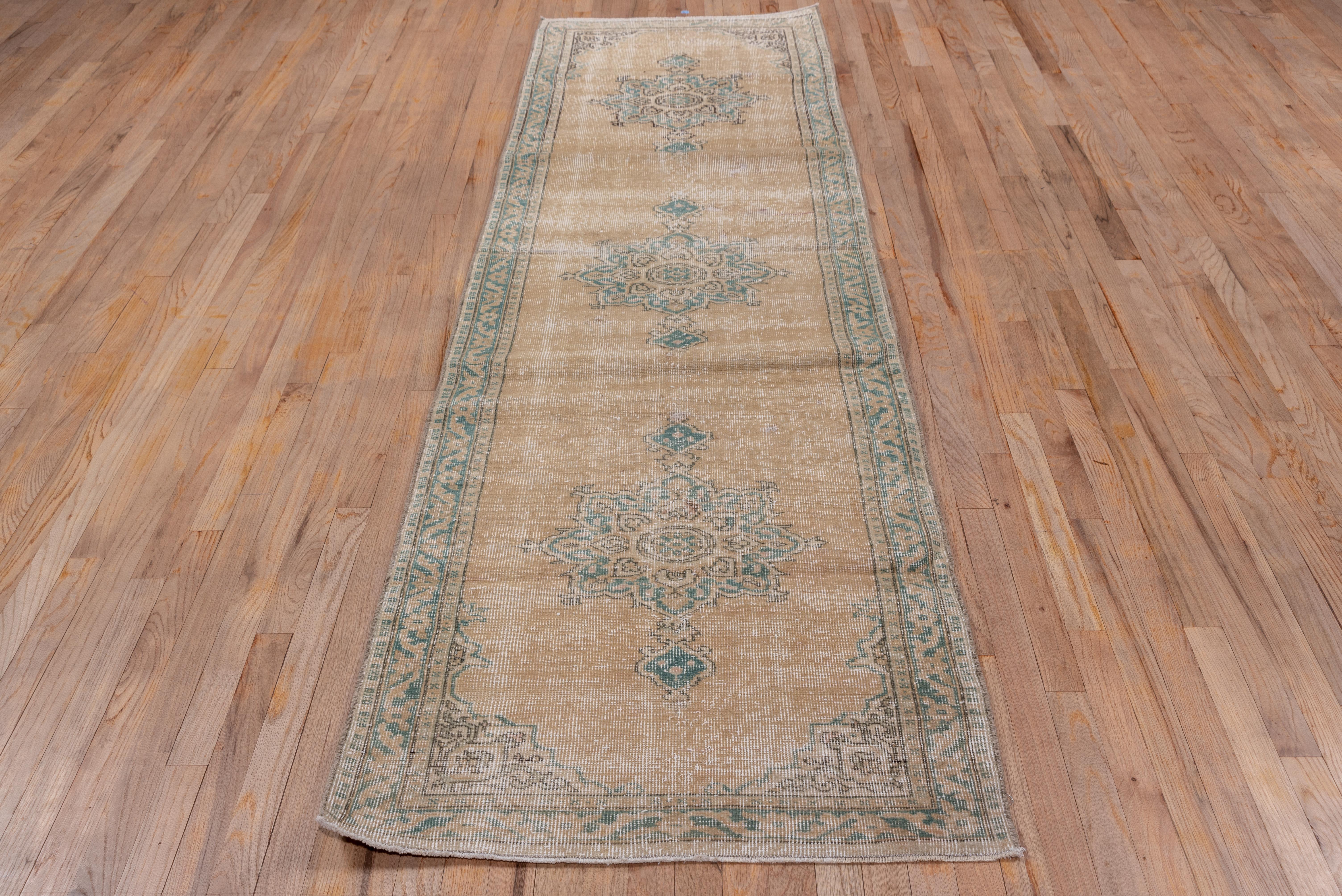 This distressed runner displays three pendanted grey-green octofoil medallions floating on an open almond ground with arabesque patterned beige corners. The grey-green narrow main border displays a stencil patterned broad vine.