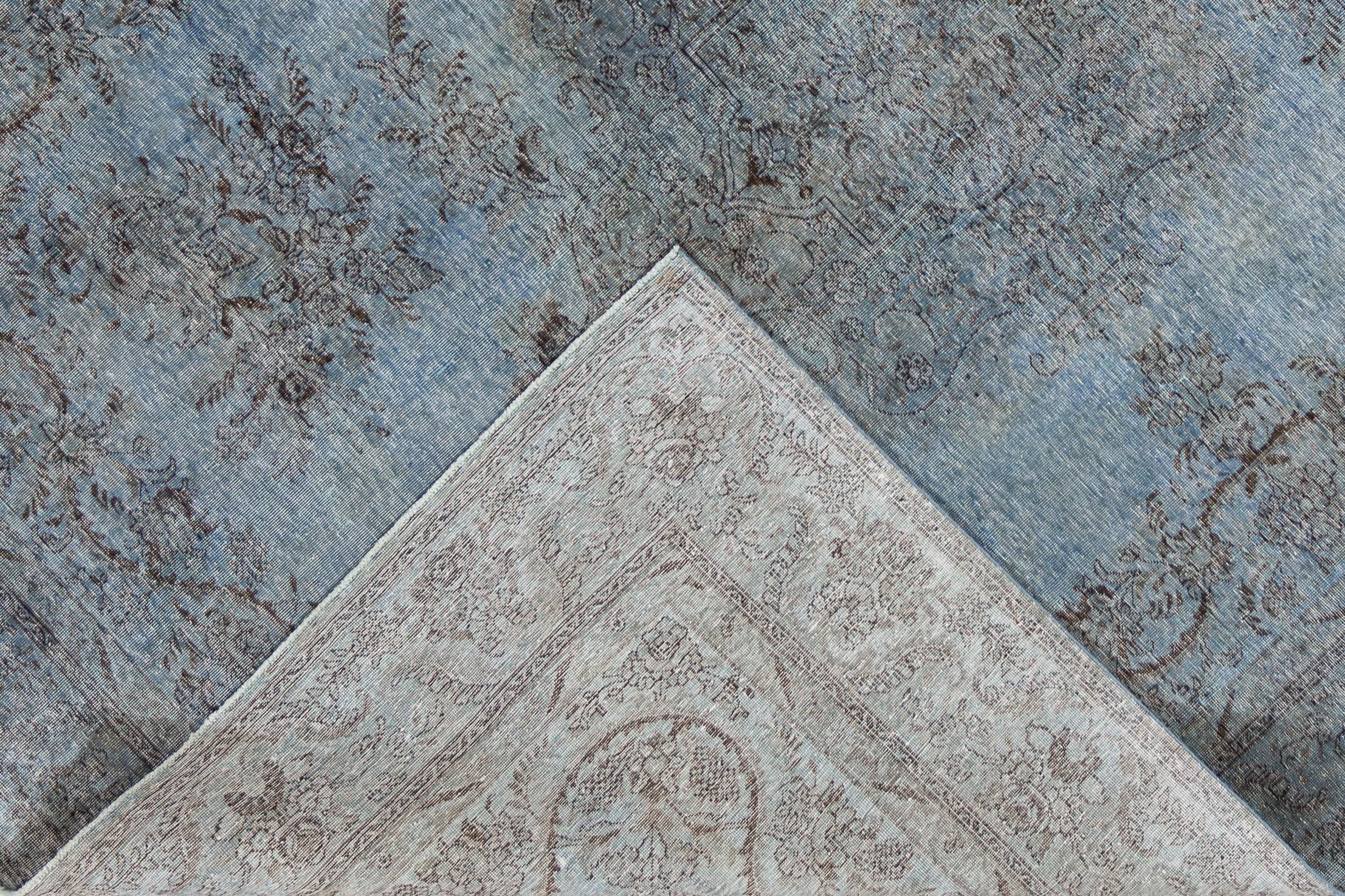 Un tapis surteint vintage vieilli avec un champ bleu denim clair et un motif floral médaillon sous-jacent. Ce tapis en laine noué à la main mesure 9'5