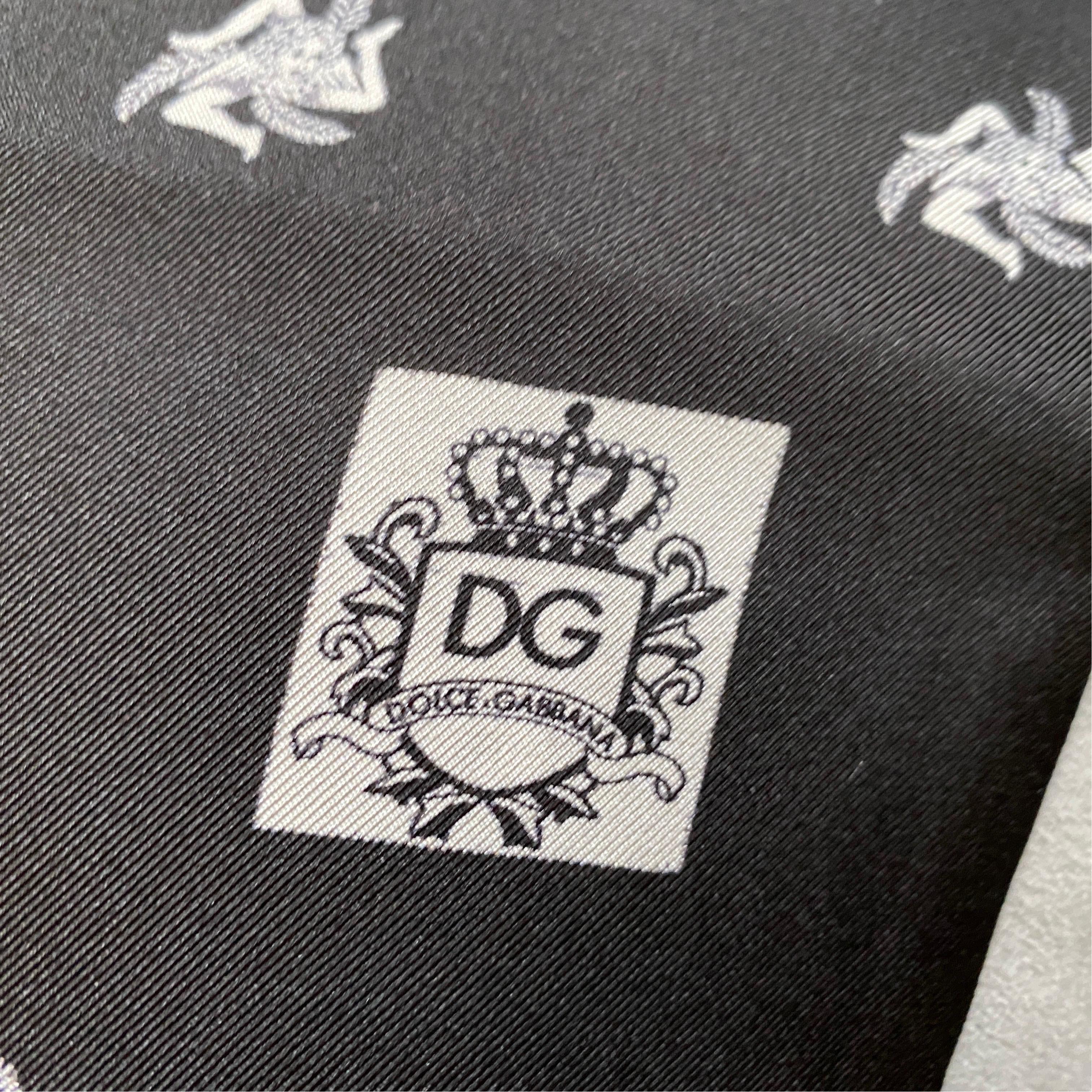 A black and white silk scarf designed and manufactured by Dolce & Gabbana with Sicilian symbols of Trinacria. The silk scarf d is a stylish and culturally significant accessory. Dolce & Gabbana is an Italian luxury fashion brand known for its bold