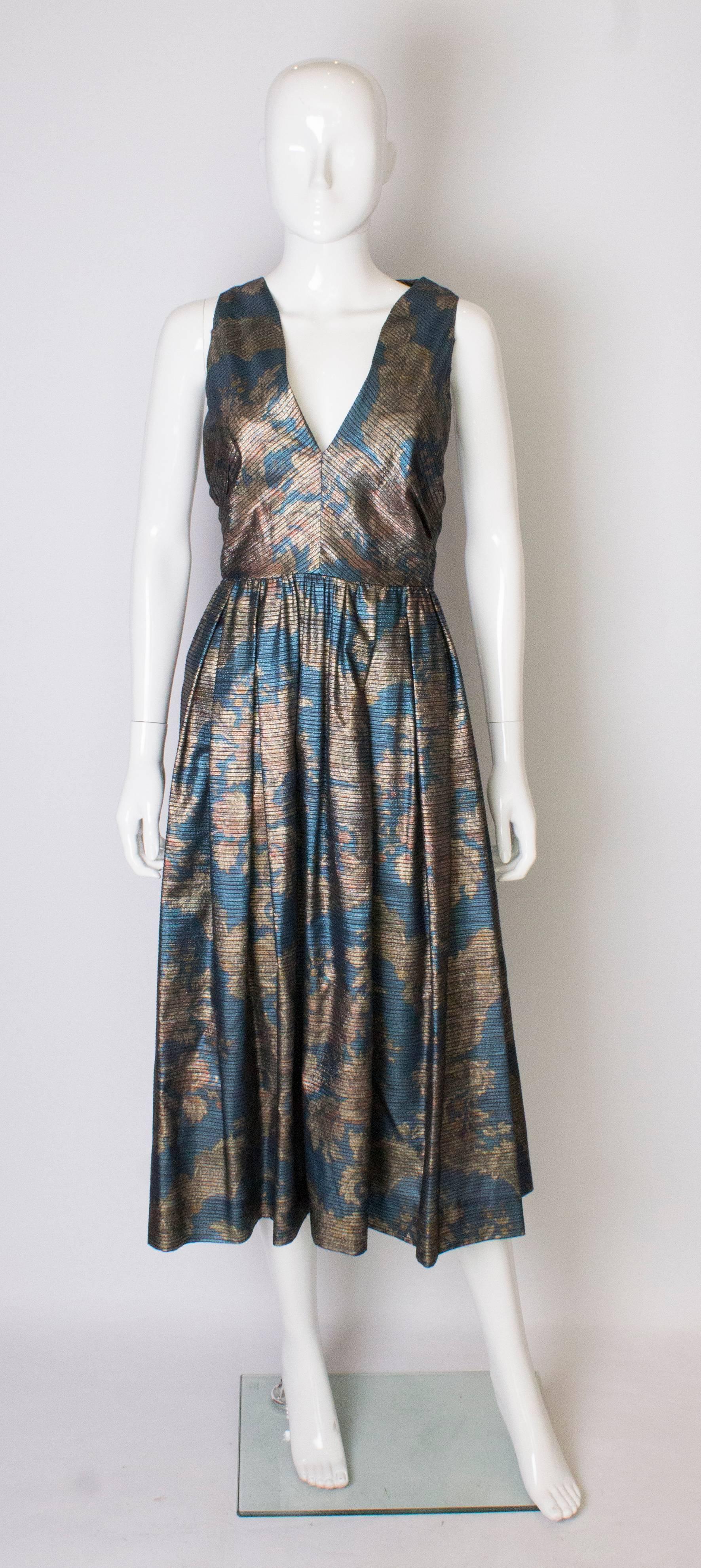 Ein wunderschönes Vintage-Kleid von Donald Campbell, in einem blauen, goldenen und rostfarbenen Stoff.
Das Kleid ist ärmellos, hat einen V-Ausschnitt und einen zentralen Reißverschluss am Rücken.