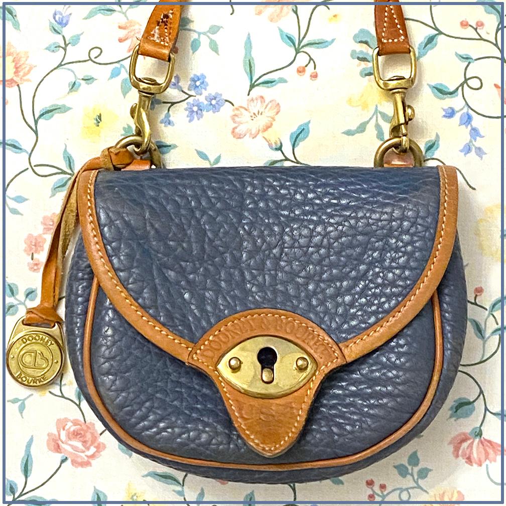 This is a late 1980s vintage DOONEY & BOURKE calvary mini crossbody bag. This denim blue pebbled all weather leather bag has English tan trim. The brass DB fob is attached. It comes with a 41 inch detachable strap and belt loop. The mini bags still