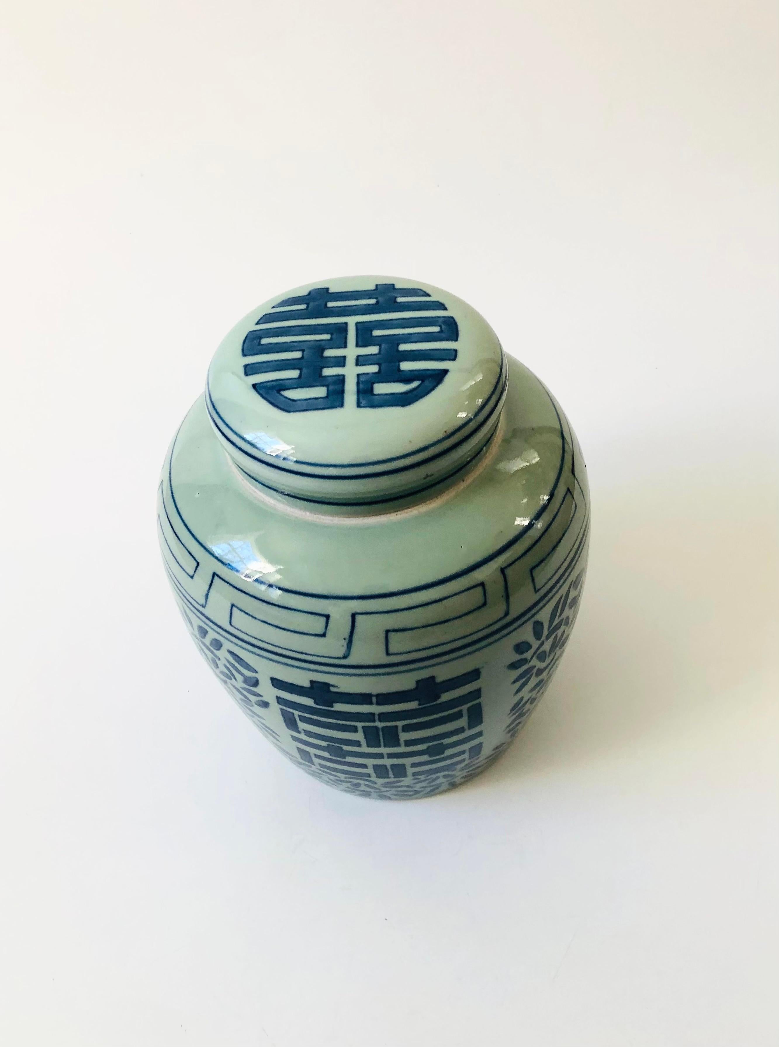 A vintage ceramic Chinese double happiness ginger jar. Beautiful hand painted details under a glossy glaze. A matching circular lid sits on the top of the jar. Large double happiness characters are painted on 2 sides with floral detailing
