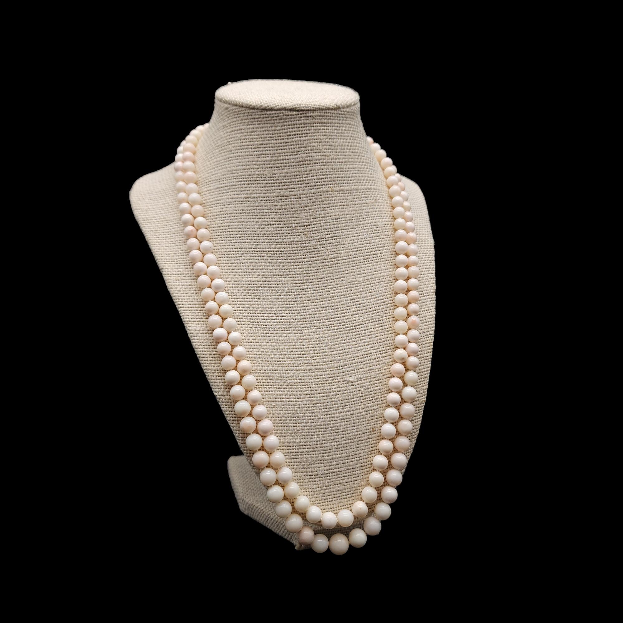 Add a touch of elegance and charm to your outfit with this vintage double strand necklace. This stunning piece features natural angel-skin coral beads in a soft off-white and pink hue The beads are hand-knotted and have a smooth, round shape. The