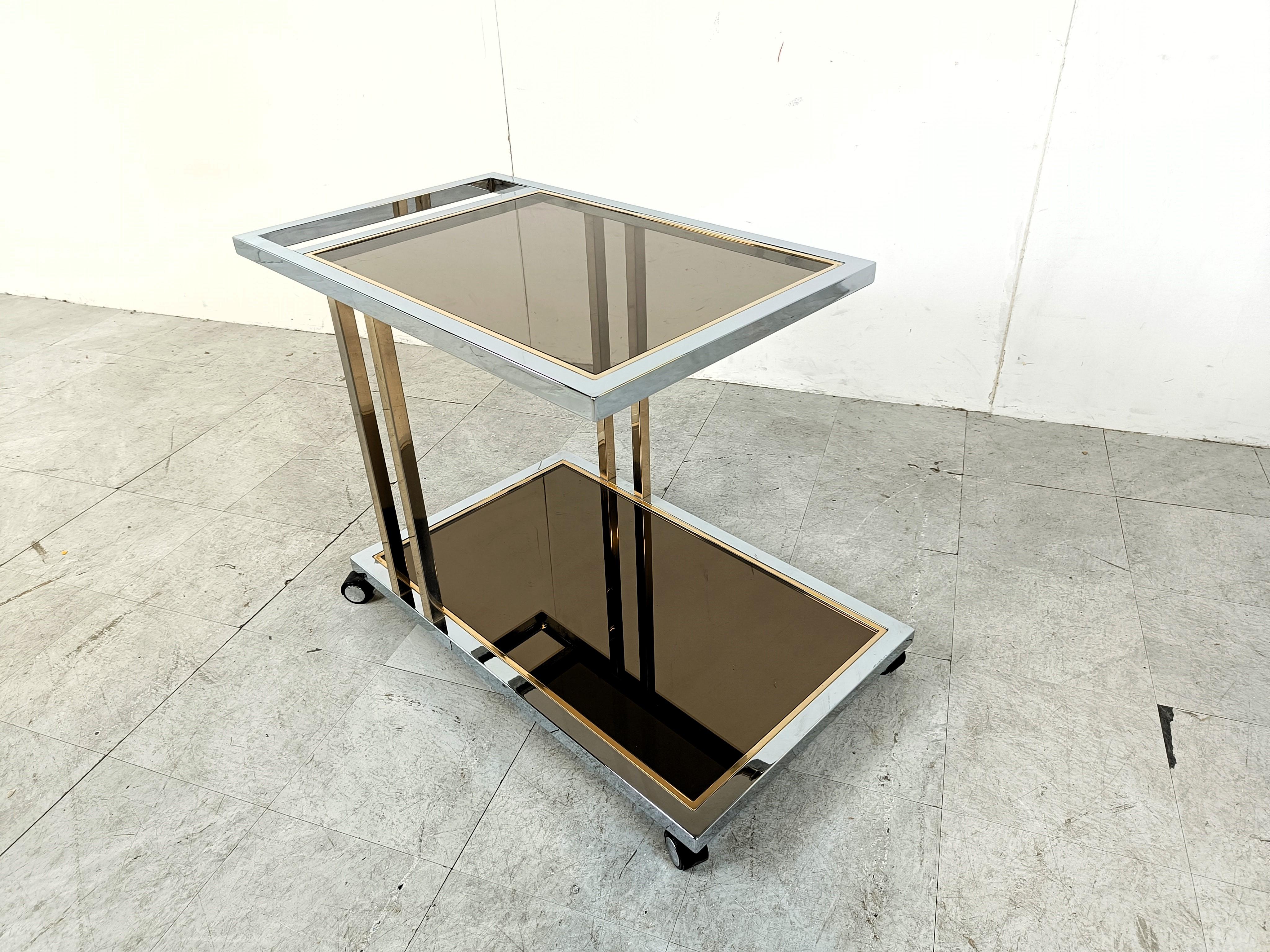 This two tier cart consists of a smoked glass top and a mirrored glass lower shelve and is made of brass and chrome.

Polished brass and chrome.

Good condition, original label still attached.

1970s - Belgium

Dimensions:

Height: