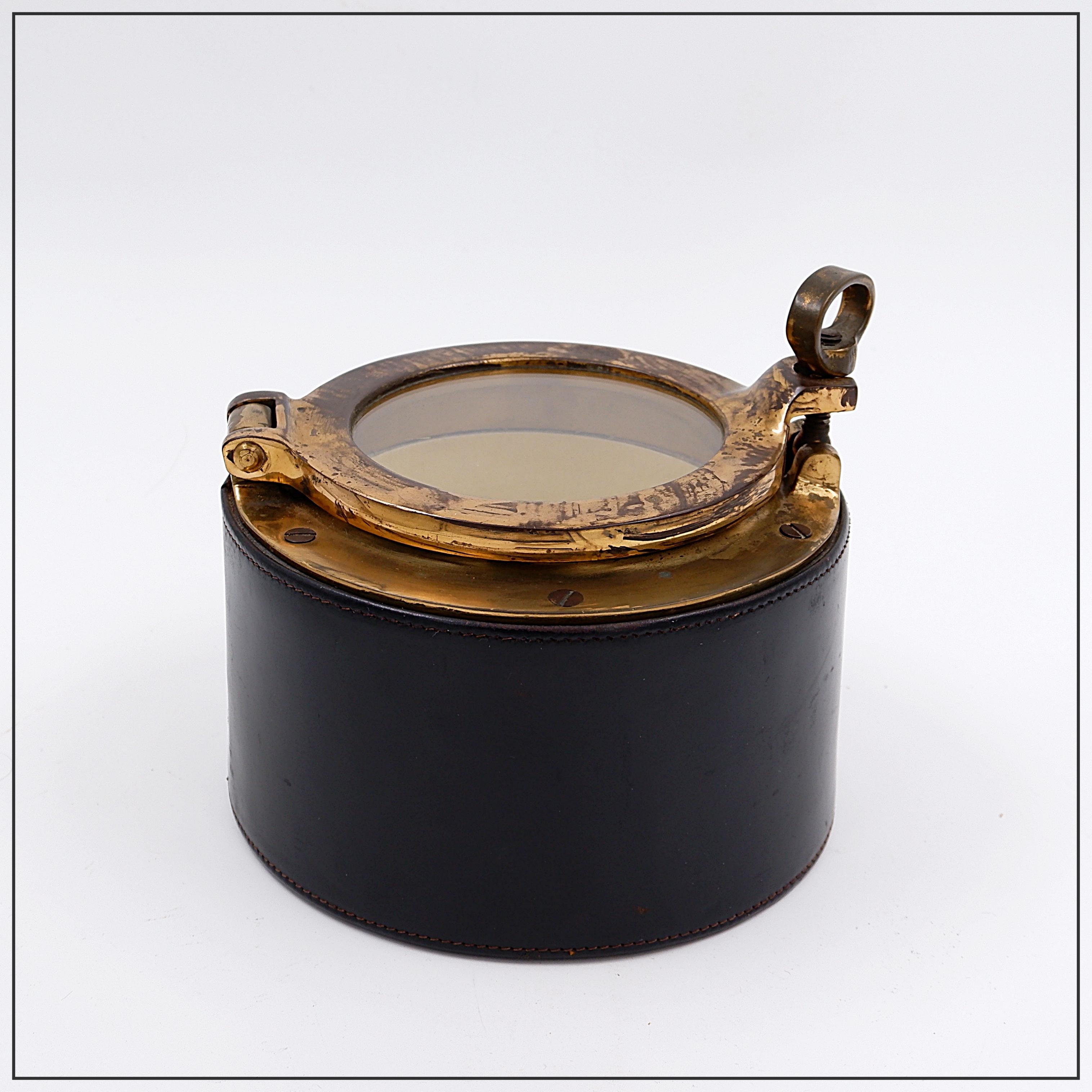 Stile Jacques Adnet - Anni '60 - Metà secolo
Misure: Ø 17cm H. 11cm
Materiali : Pelle - Ottone - Vetro 
Un'elegante scatola in ottone della metà del XX secolo a forma di oblò con rivestimento in pelle cucito, nello stile di Jacques Adnet.