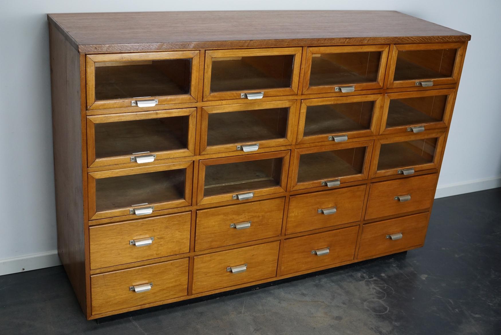 This haberdashery cabinet was produced during the 1950s in the Netherlands. This piece features 20 drawers in beech with glass fronts and metal handles. It was originally used in a luxury warehouse in the city of Maastricht. The interior dimensions