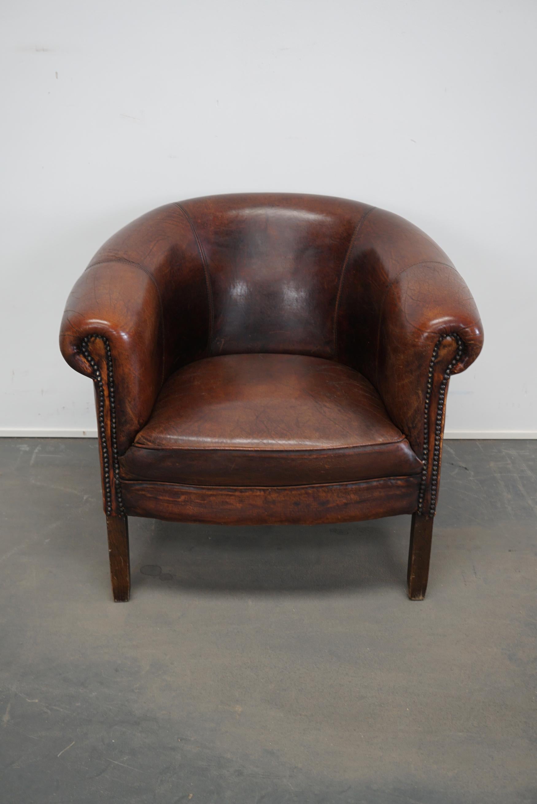 This burgundy-colored leather club chair comes from the Netherlands. It is upholstered with burgundy-colored leather and features metal rivets and wooden legs.