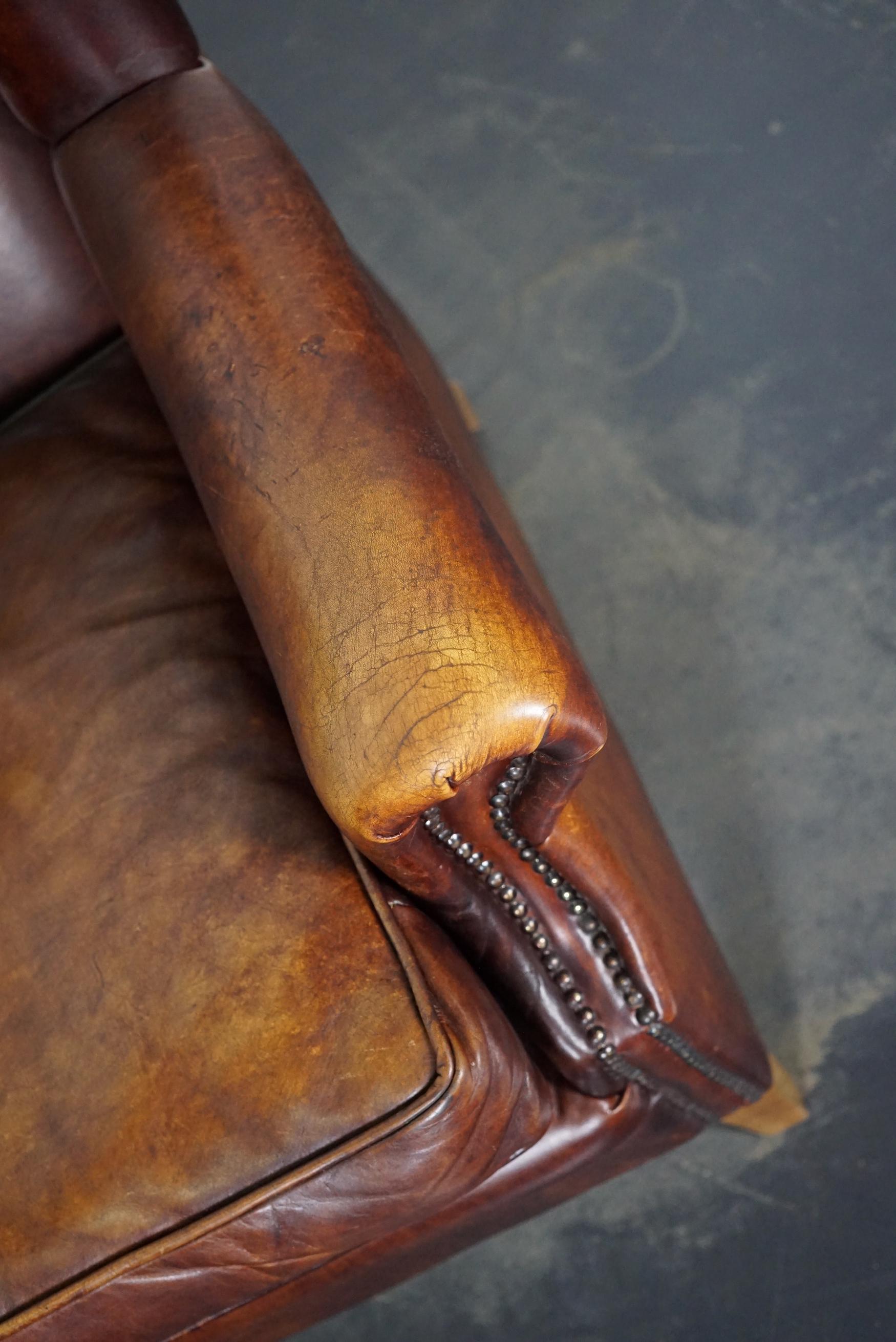 This burgundy-colored leather club chair comes from the Netherlands. It is upholstered with burgundy-colored leather and features metal rivets and wooden legs.