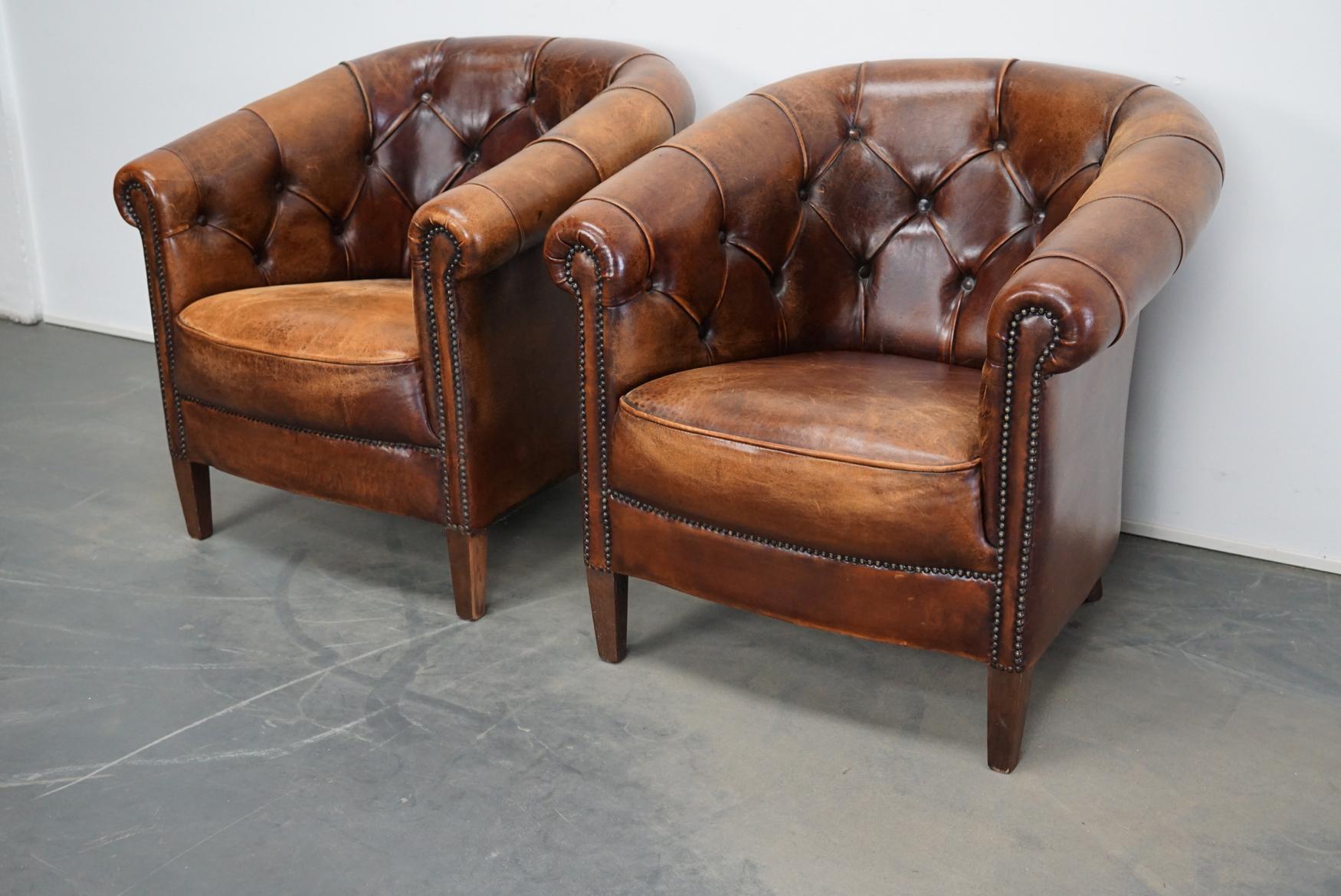 This pair of cognac-colored leather club chairs come from the Netherlands. They are upholstered with cognac-colored leather and feature metal rivets and wooden legs.